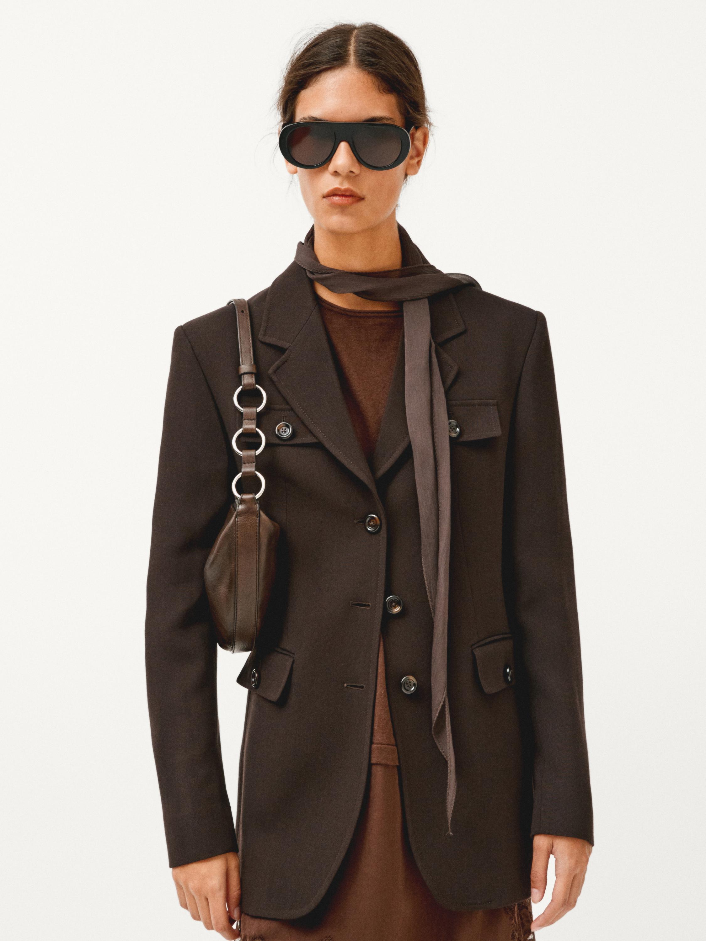 Brunt blazersæt med klaplommer og knapper, tyndt brunt tørklæde og mørk skuldertaske.