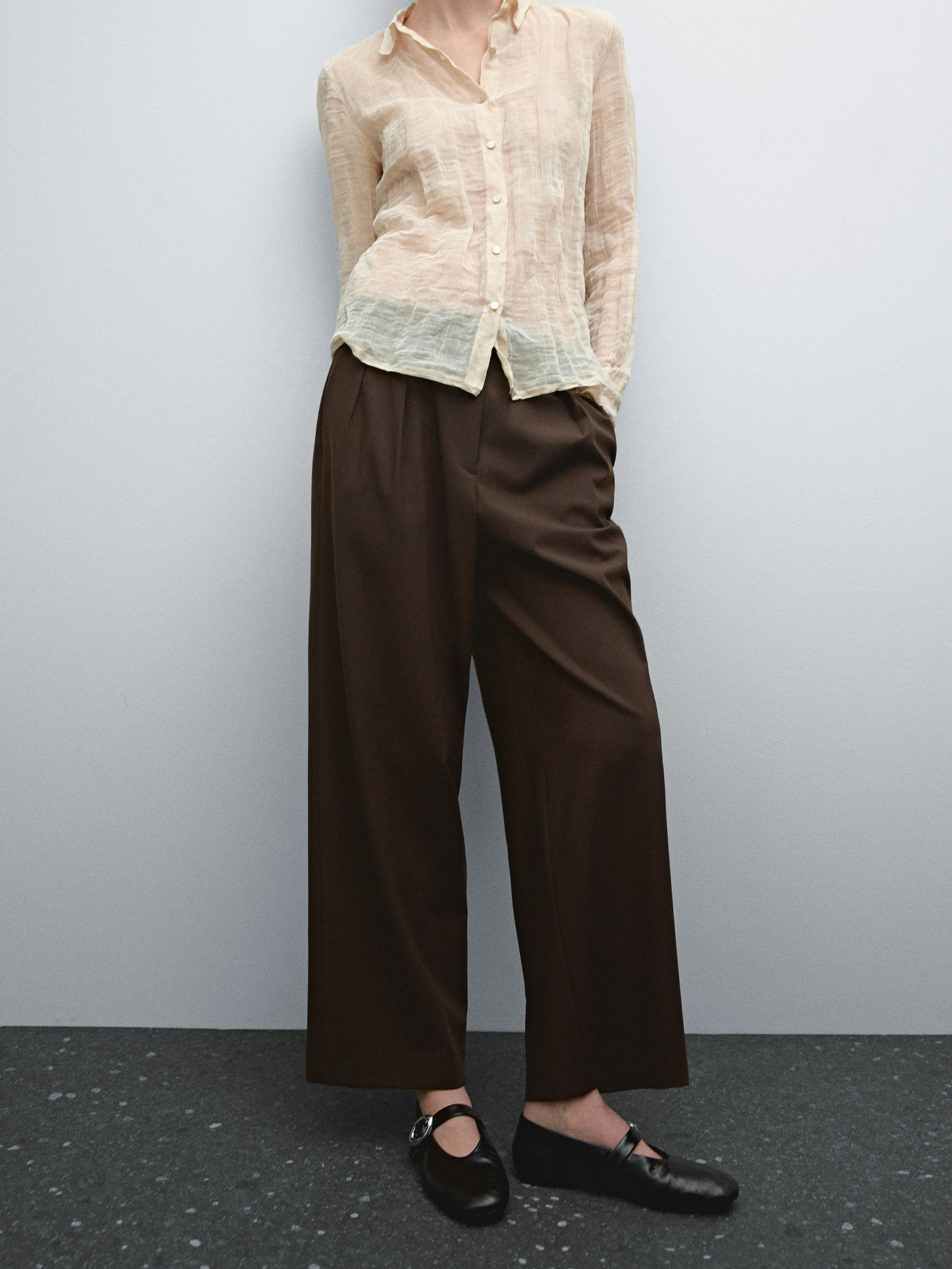 Conjunto de camisa beige semitransparente y pantalones marrones anchos con zapatos negros.