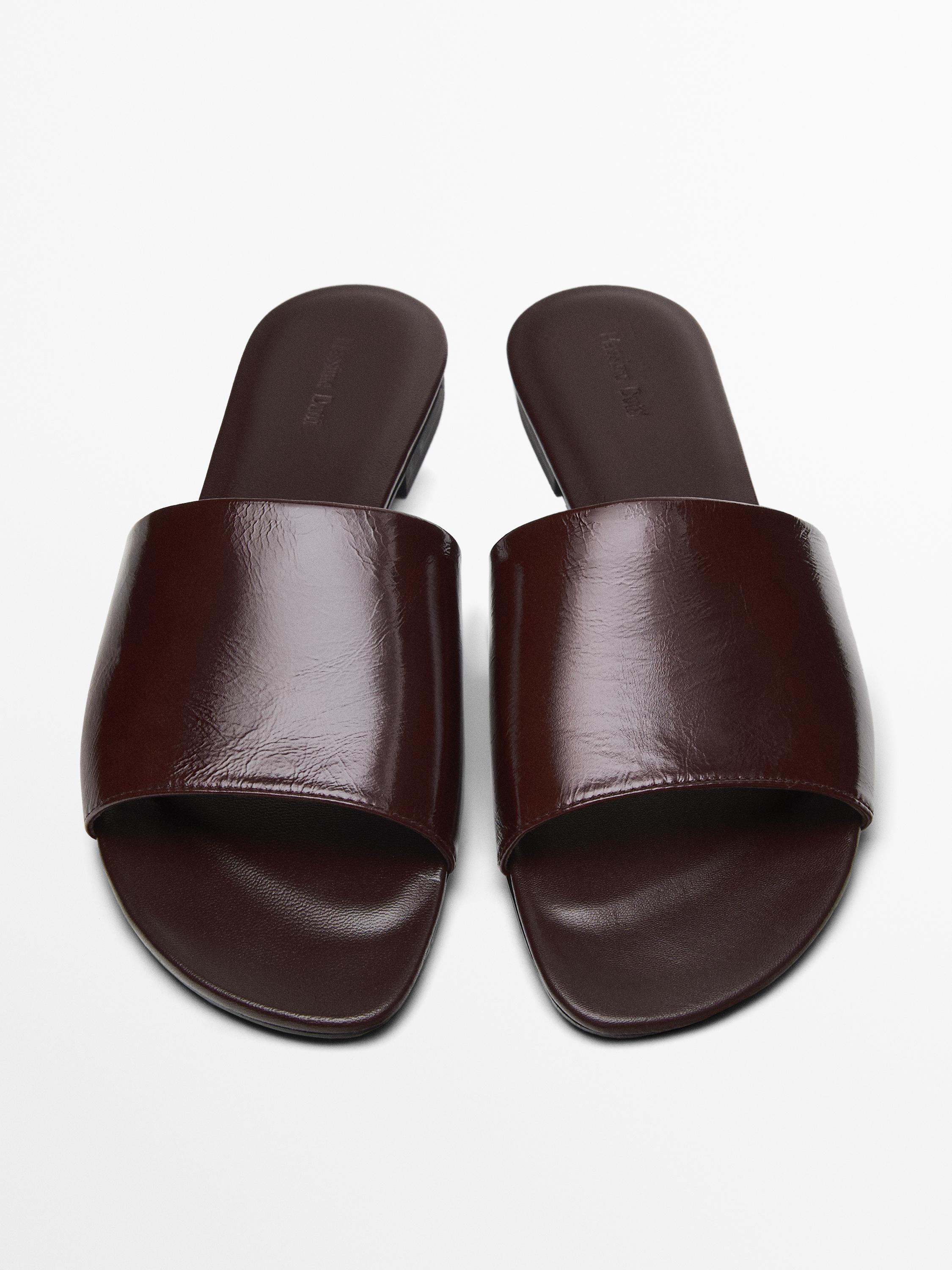 Front view of dark brown flat sandals with open design and wide strap on top.