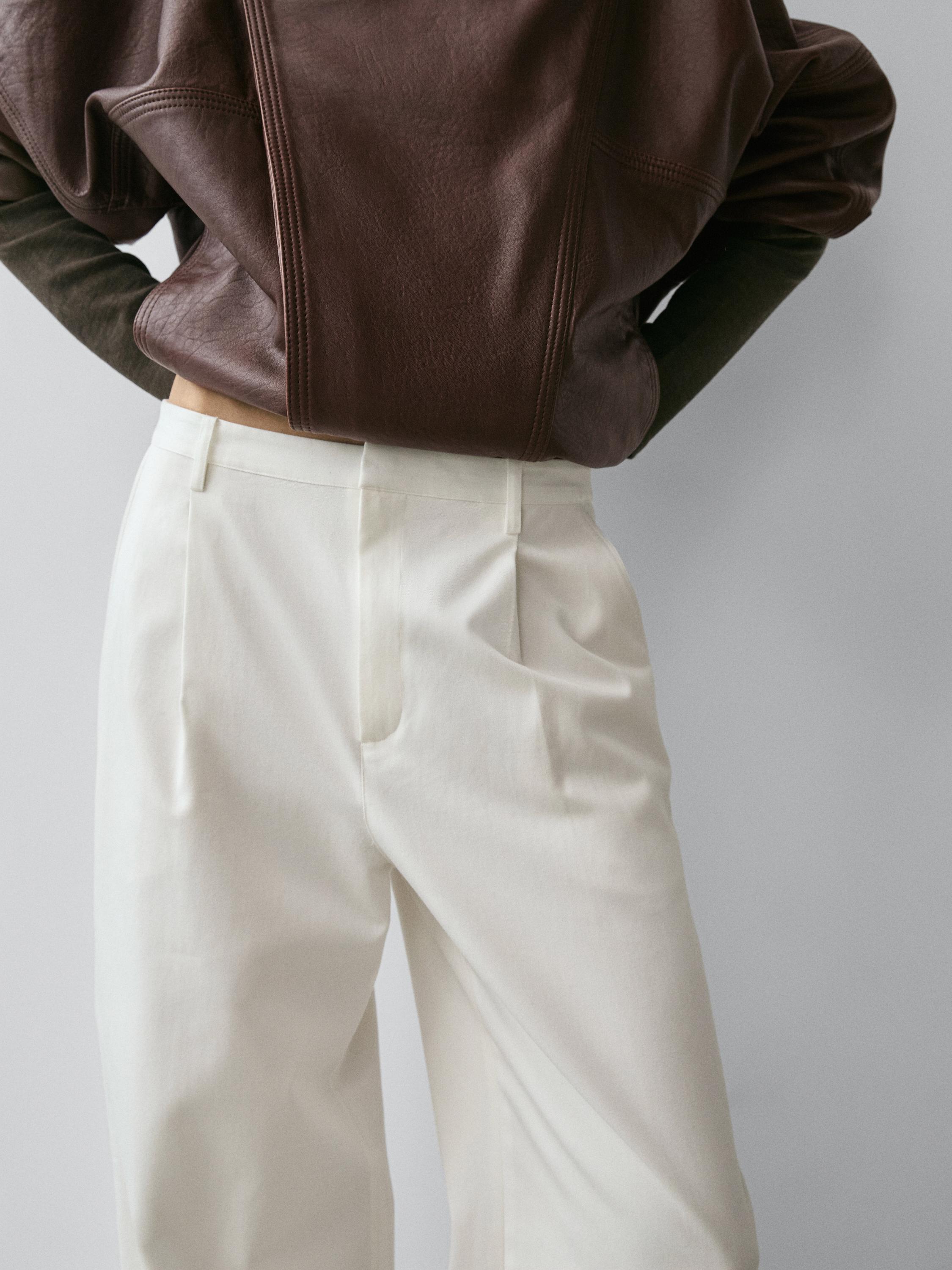 Mid-shot of white pants with pleats and side pockets.