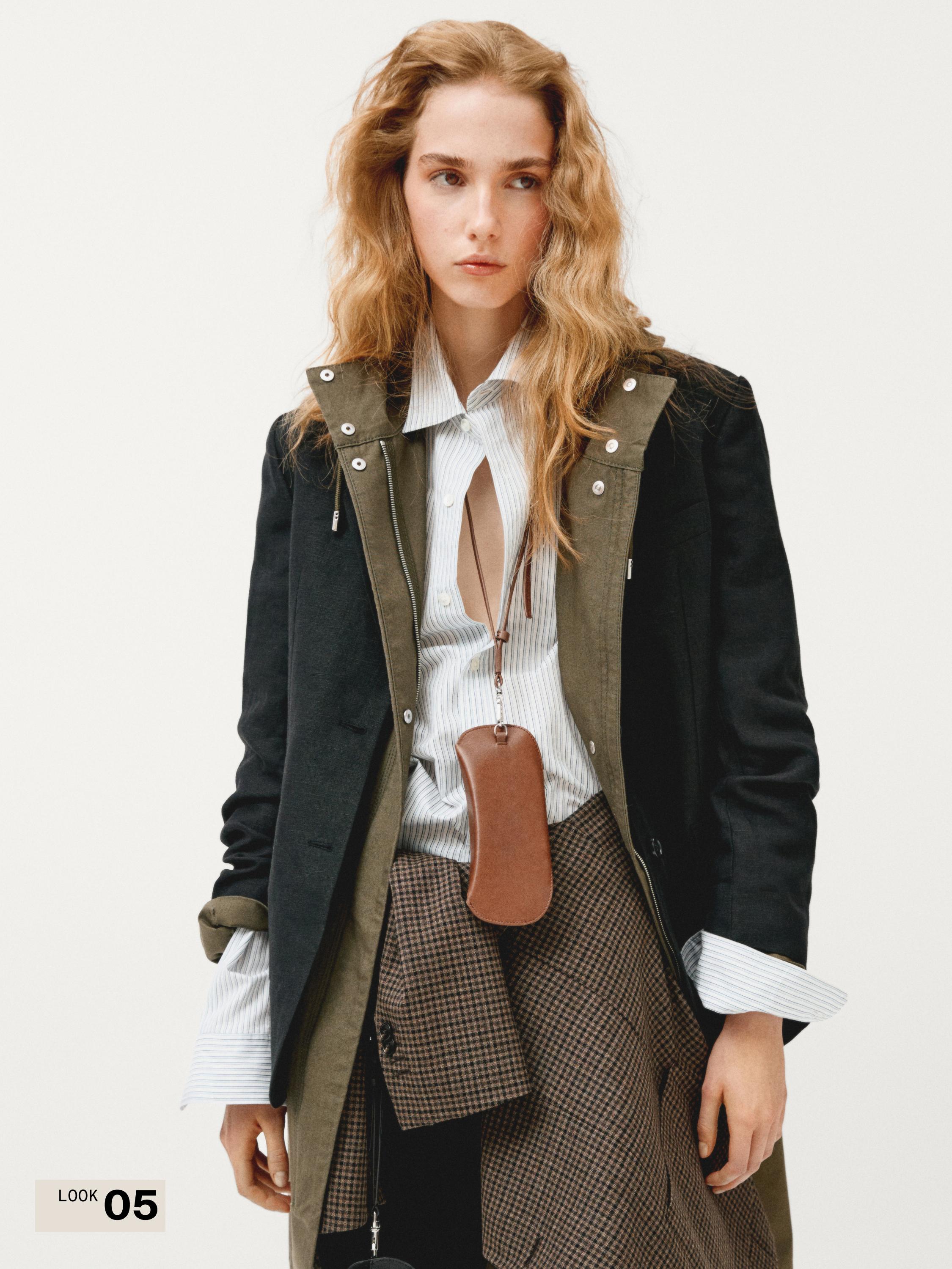 طقم جاكيت أسود وأخضر بأزرار، قميص مخطط، تنورة بنية كاروهات، وحقيبة بنية متدلية.