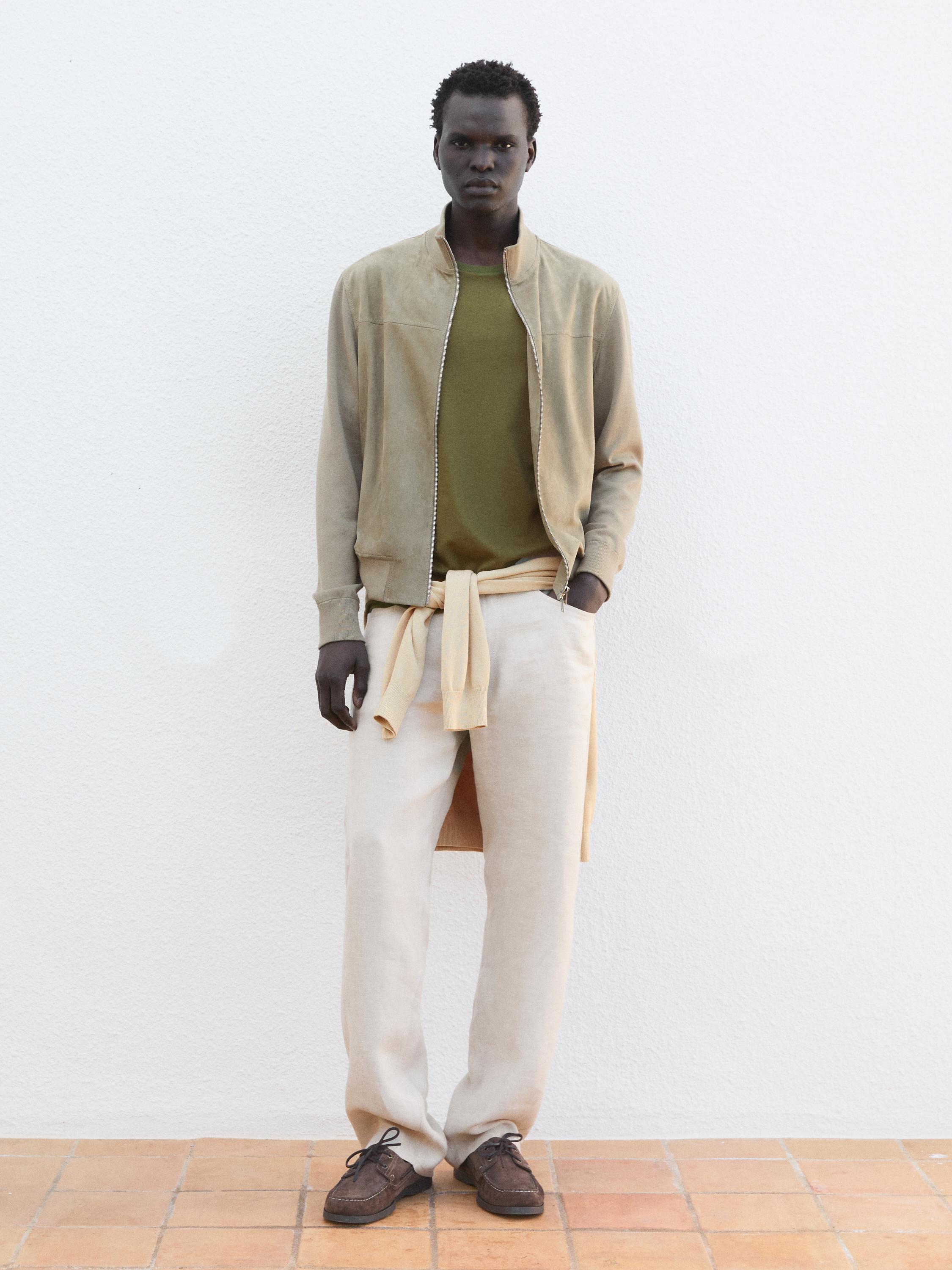 Conjunto de chaqueta beige con cierre, playera verde olivo, pantalones beige y zapatos marrones.