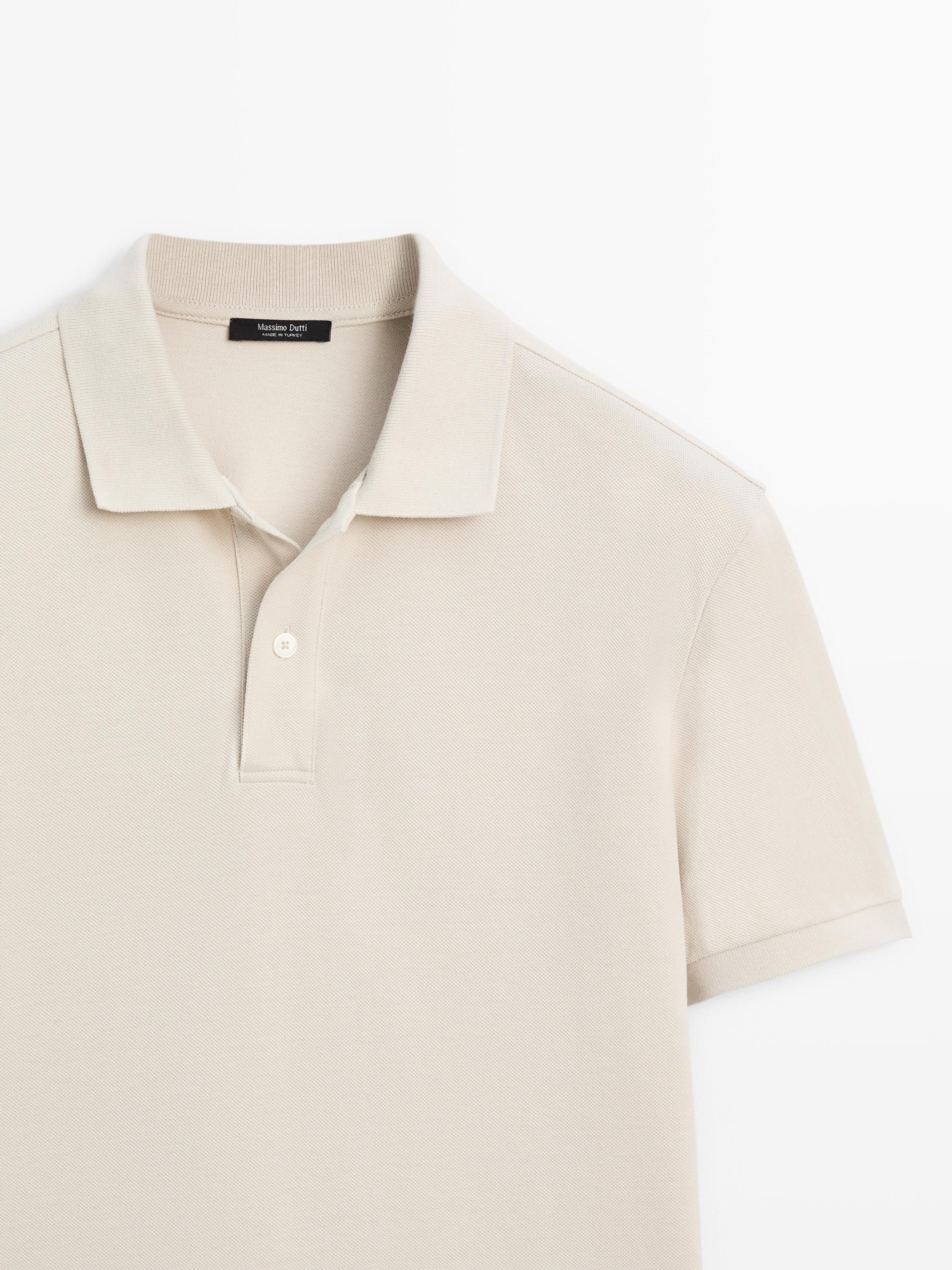 Primer plano de polo piedra de manga corta con cuello clásico y botonadura parcial.