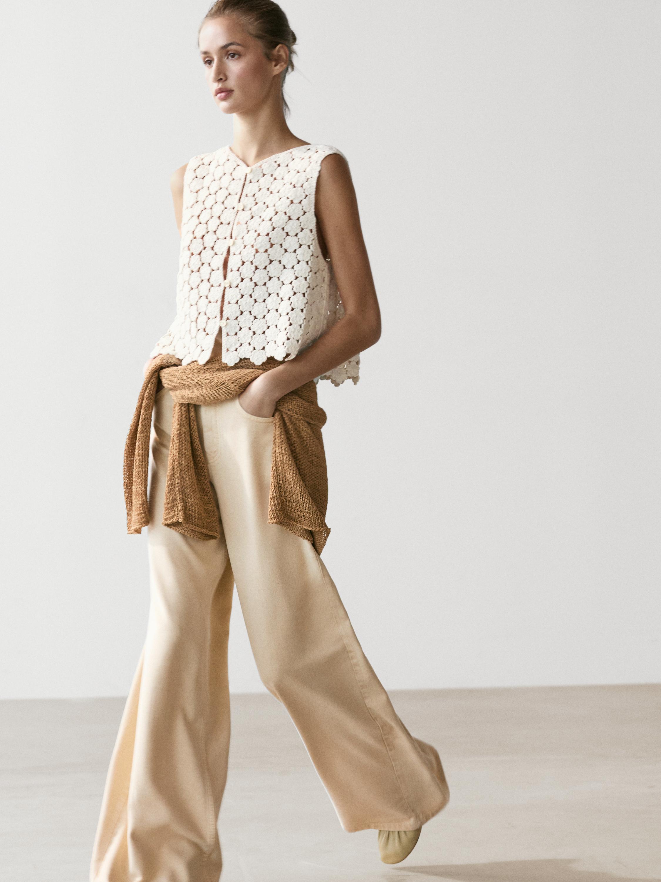 Conjunto de chaleco crochet crudo con detalle de flores y pantalones anchos beige.