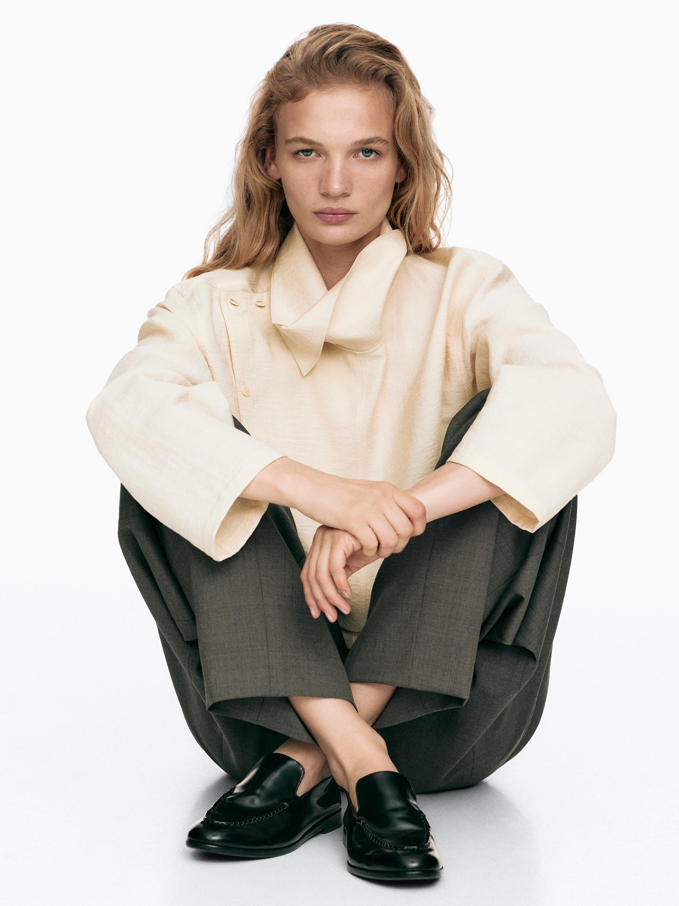 Ensemble composé d'un chemisier col roulé beige, d'un pantalon large gris et de mocassins noirs.