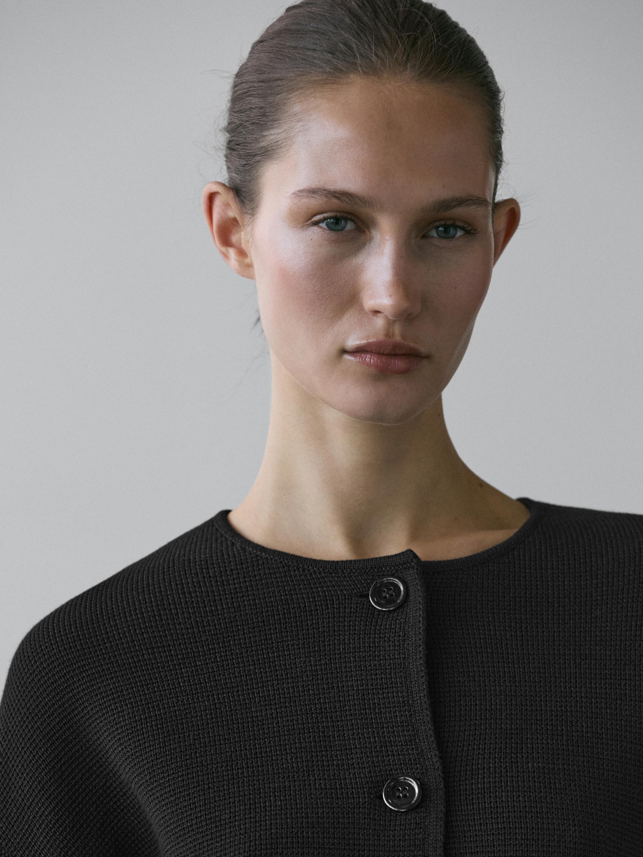 لقطة متوسطة لكارديجان أسود بياقة مستديرة وأزرار أمامية ظاهرة.