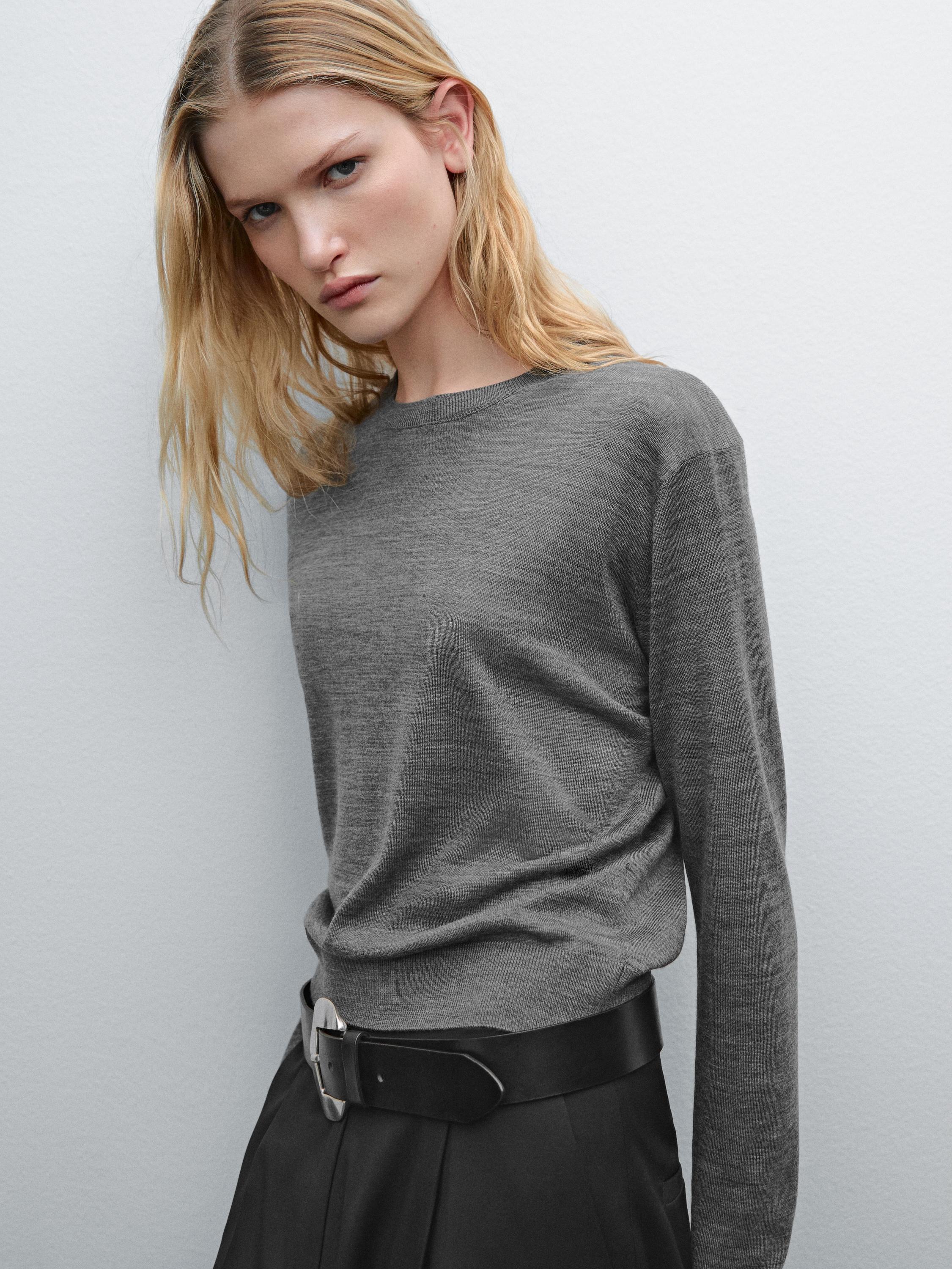 Gros plan d'un pull gris à manches longues avec une ceinture noire visible.