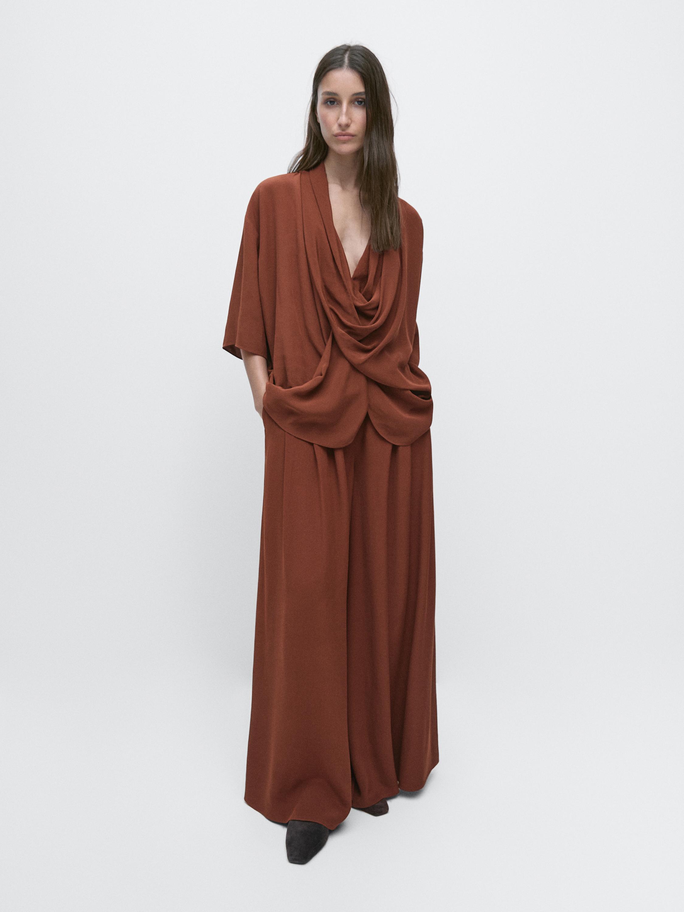 Orange blouse set with a draped neckline and matching wide-leg pants with side pockets.