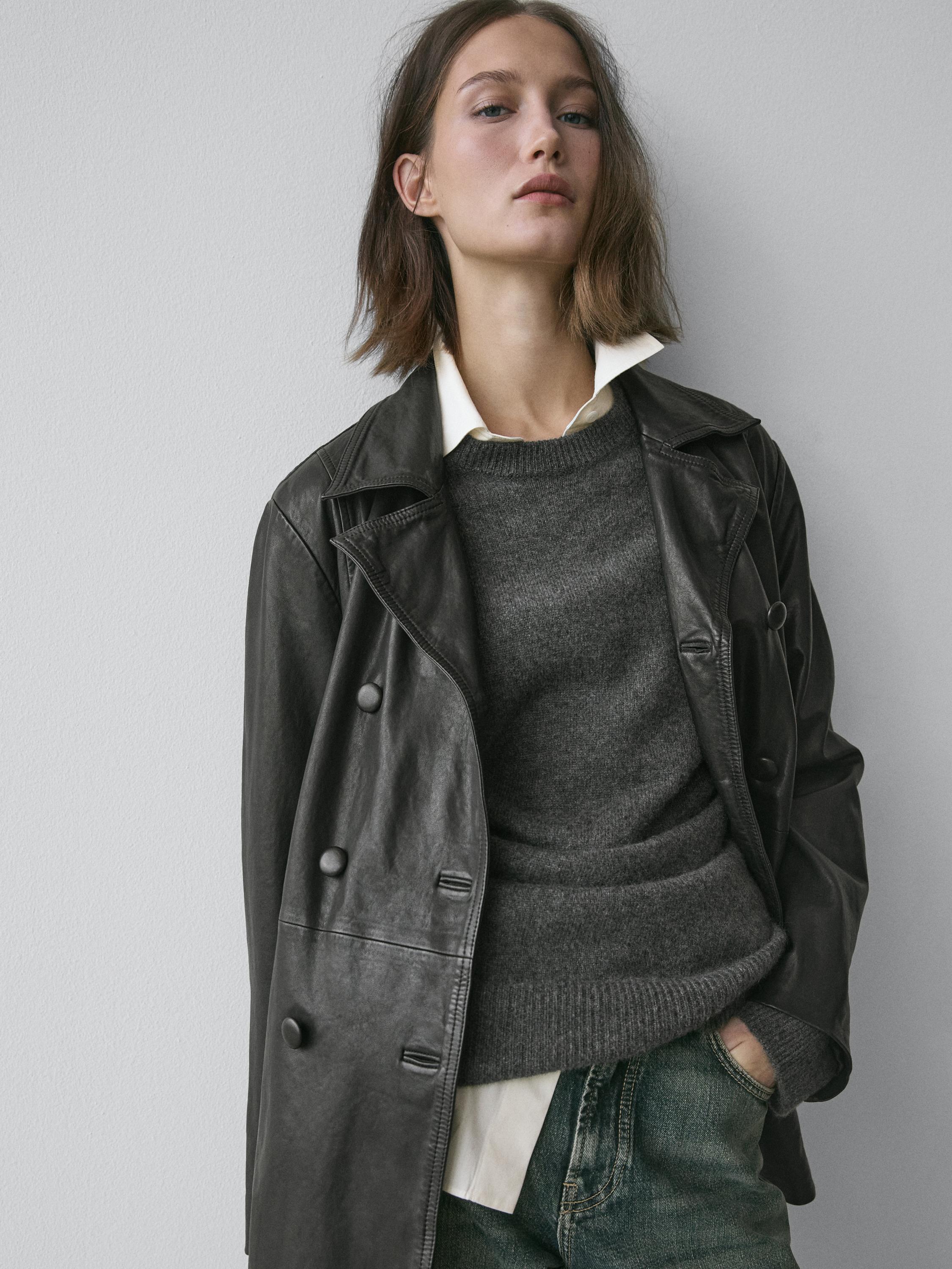 طقم يتكون من سترة سوداء بأزرار كبيرة، وكنزة صوفية رمادية، وقميص أبيض، وبنطلون جينز.