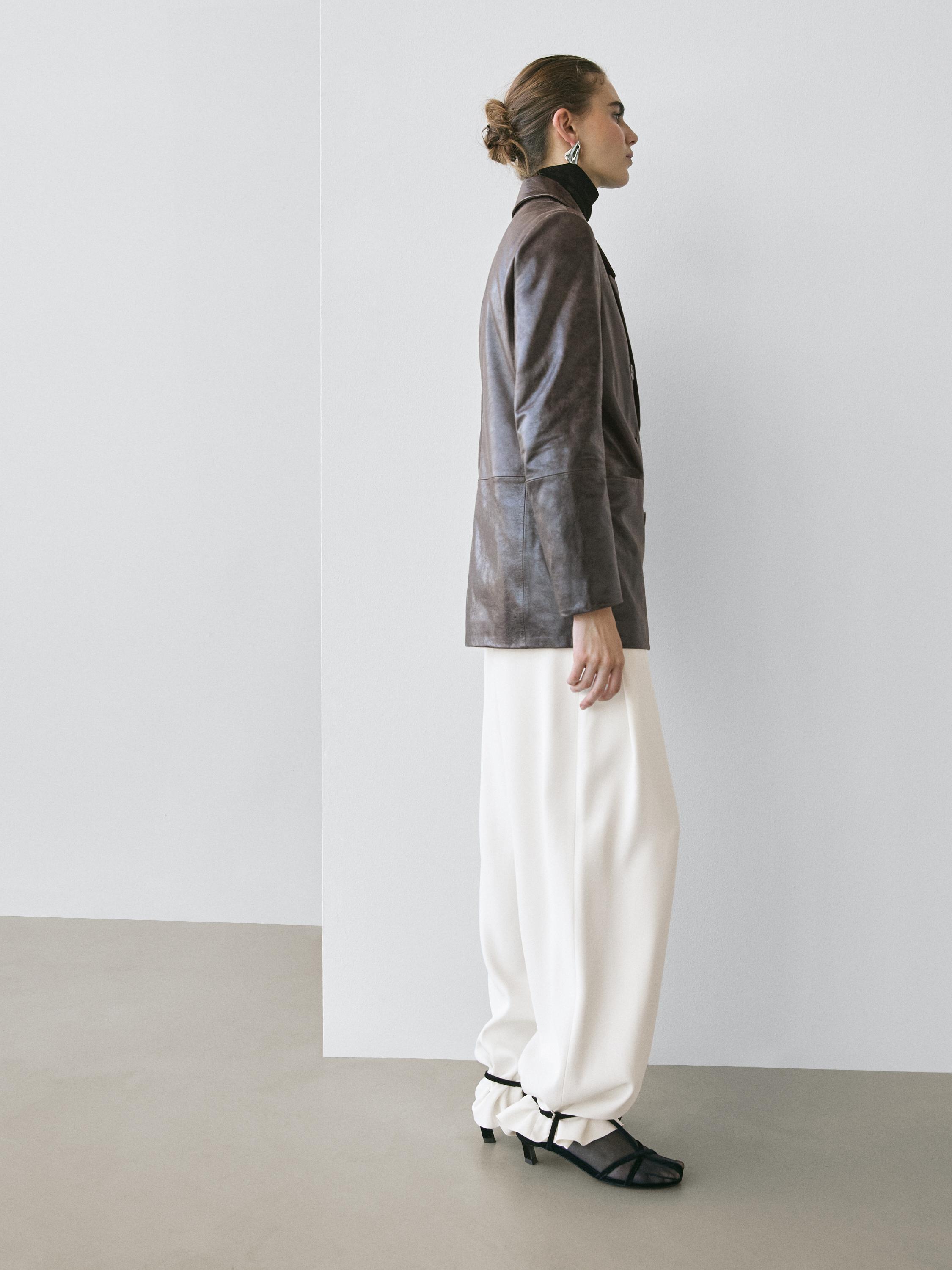 Ensemble composé d'une veste marron à boutons et poches latérales, d'un pantalon blanc ample et de sandales noires à talons.