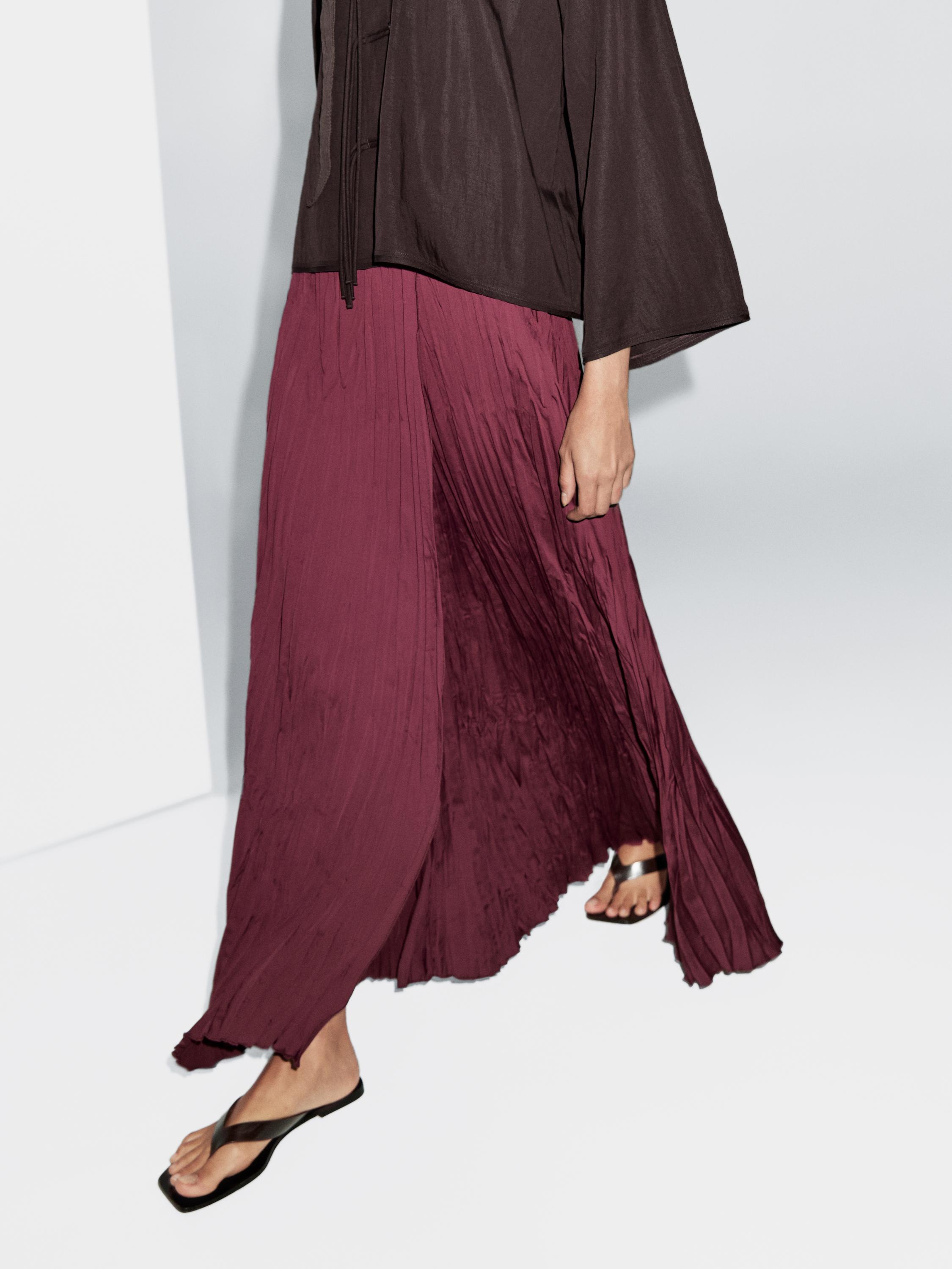 Medium shot of long burgundy pleated skirt and black long-sleeved blouse.