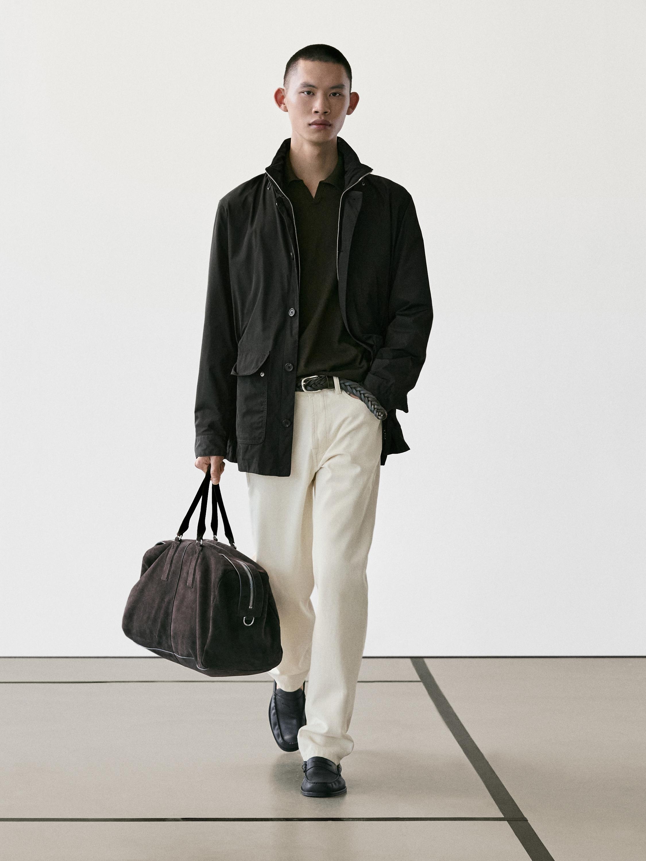 ชุดประกอบด้วยเสื้อแจ็คเก็ตสีดำ, เสื้อโปโลสีเข้ม, กางเกงขายาวสีเบจ และรองเท้าสีดำ กระเป๋าถือสีน้ำตาลเข้ม