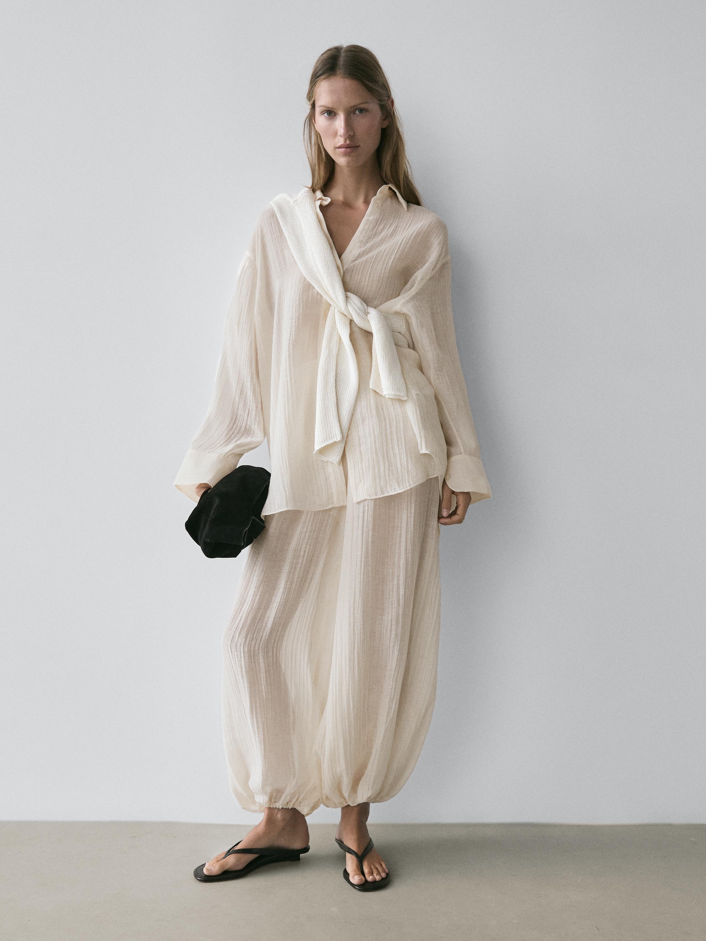 Conjunto de blusa y pantalón beige semitransparentes con textura plisada, blusa con lazo y pantalón con puños elásticos.