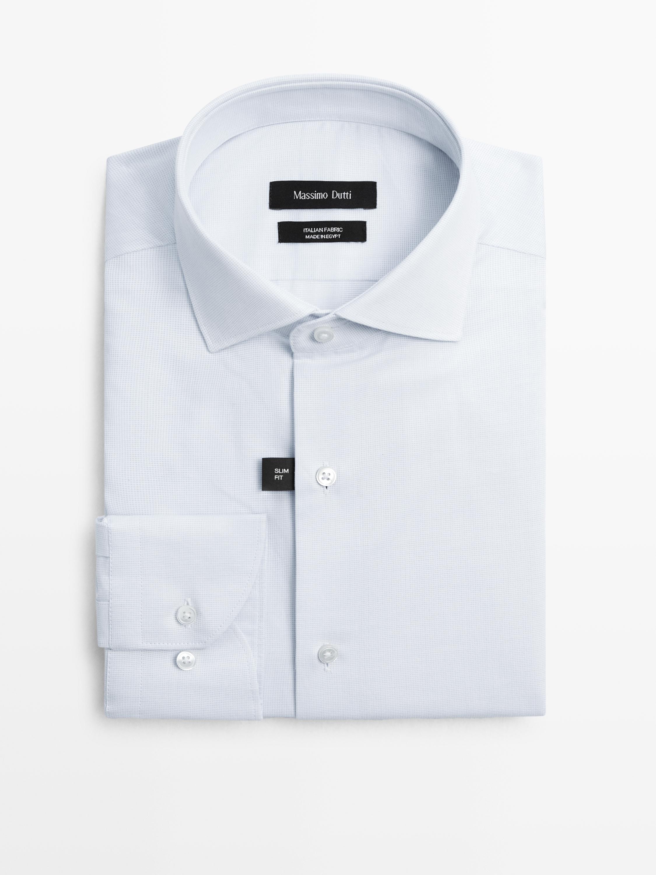 „Vorderansicht eines hellblauen Langarmhemdes, Etikett „Slim Fit“, klassischer Kragen, Manschetten mit Knöpfen.“