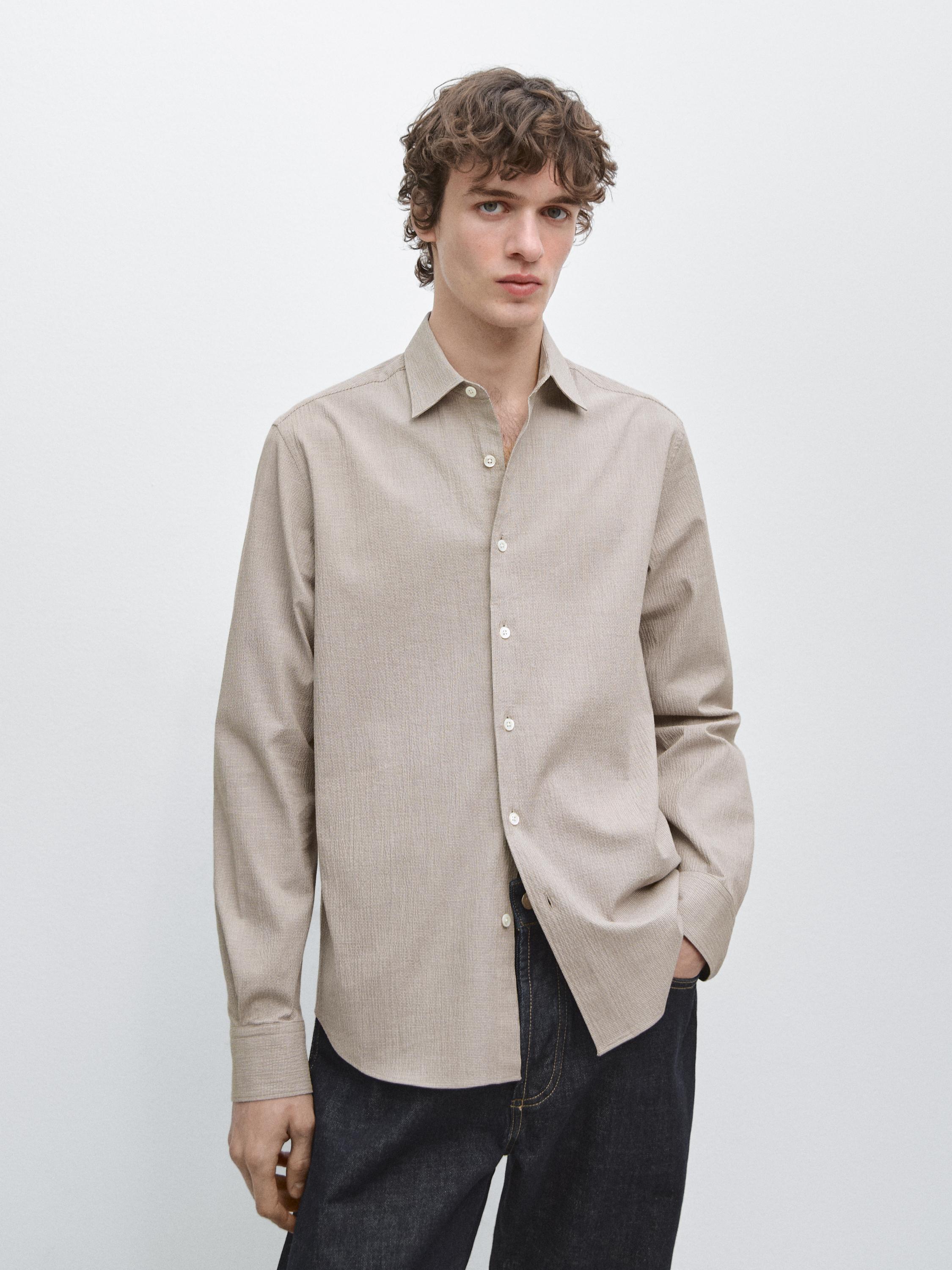 Conjunto de camisa beige de manga larga con botones frontales y cuello clásico, combinada con pantalones oscuros.