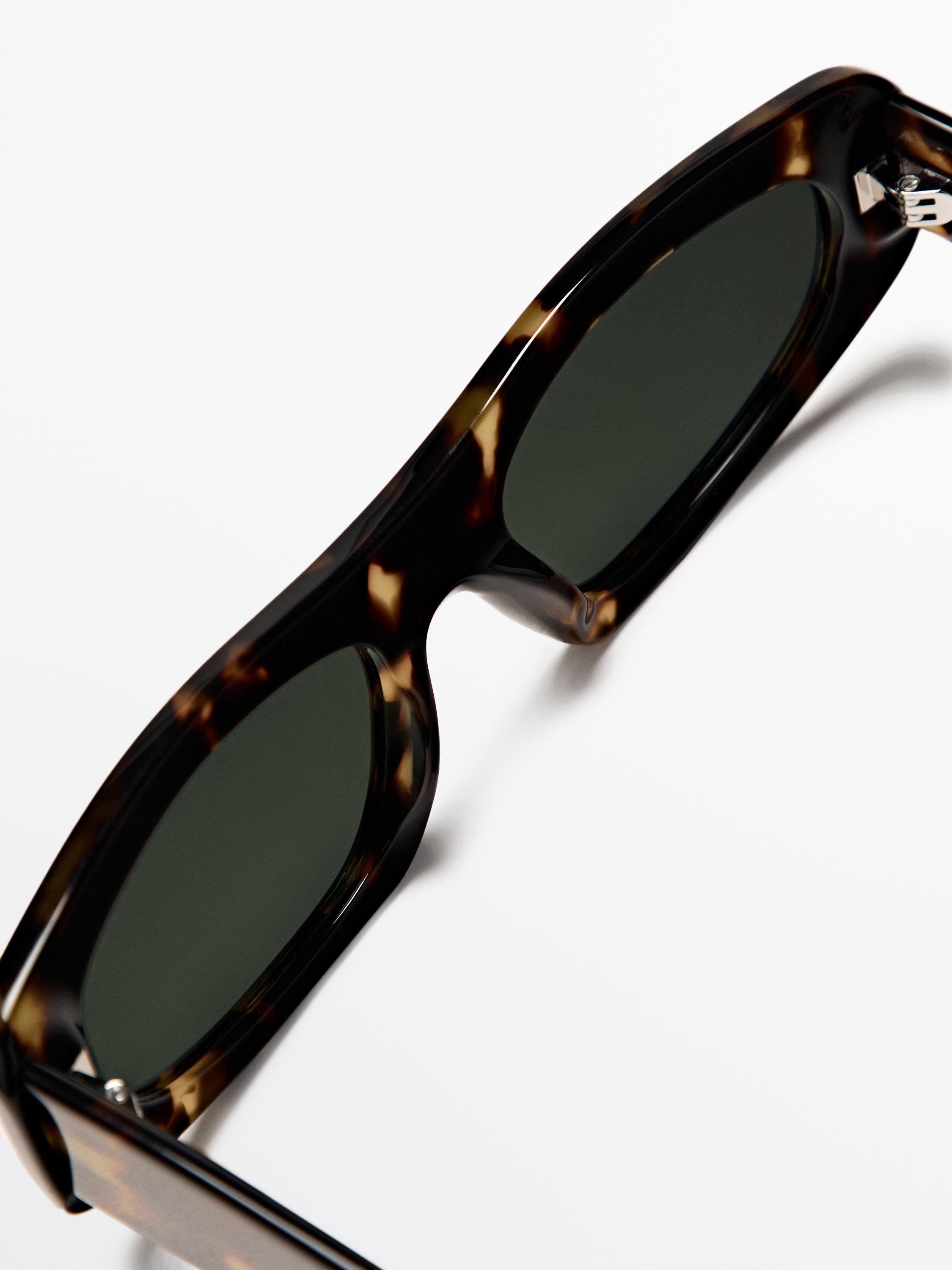 Gros plan sur des lunettes de soleil ovales marron avec une monture mouchetée et des verres foncés.