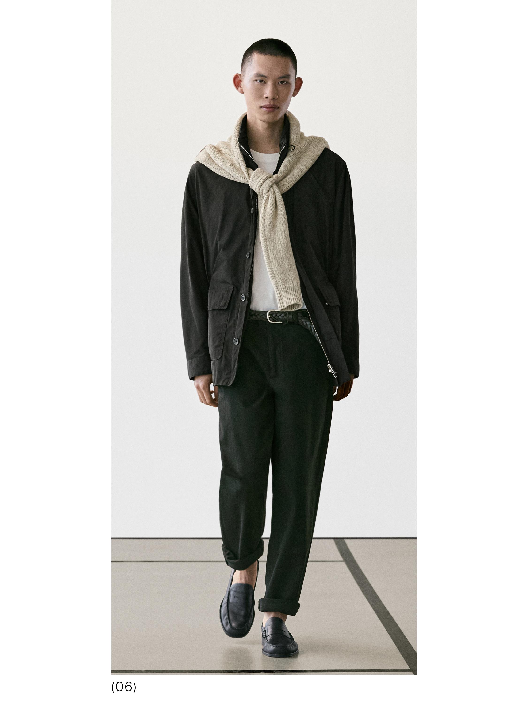 Conxunto de chaqueta negra con petos, pantalóns negros, camiseta branca e xersei beixe atado ao pescozo. Zapatos negros.