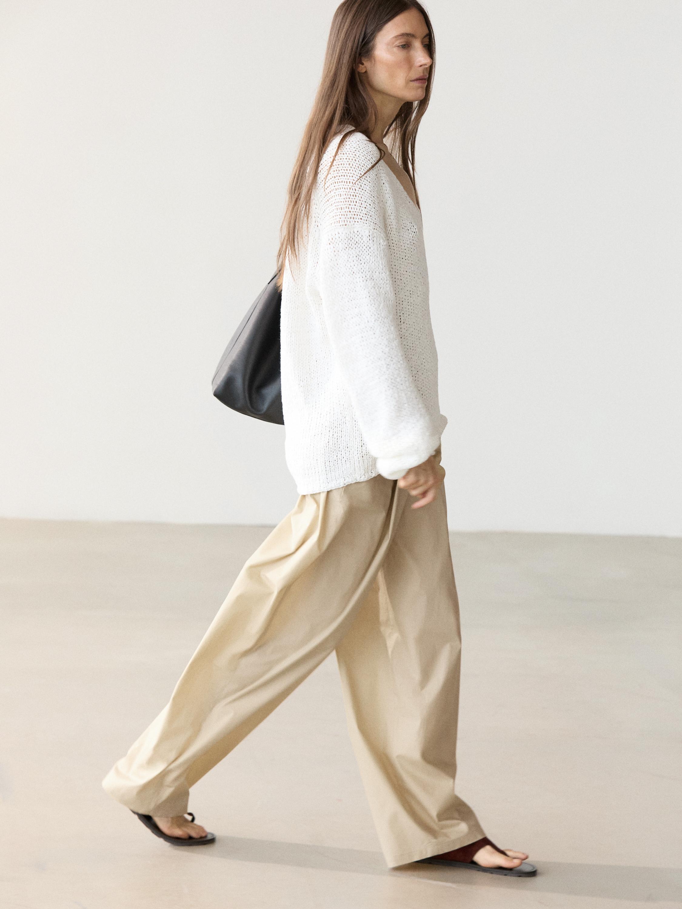 Set van witte opengewerkte trui met V-hals en beige wijde broek.