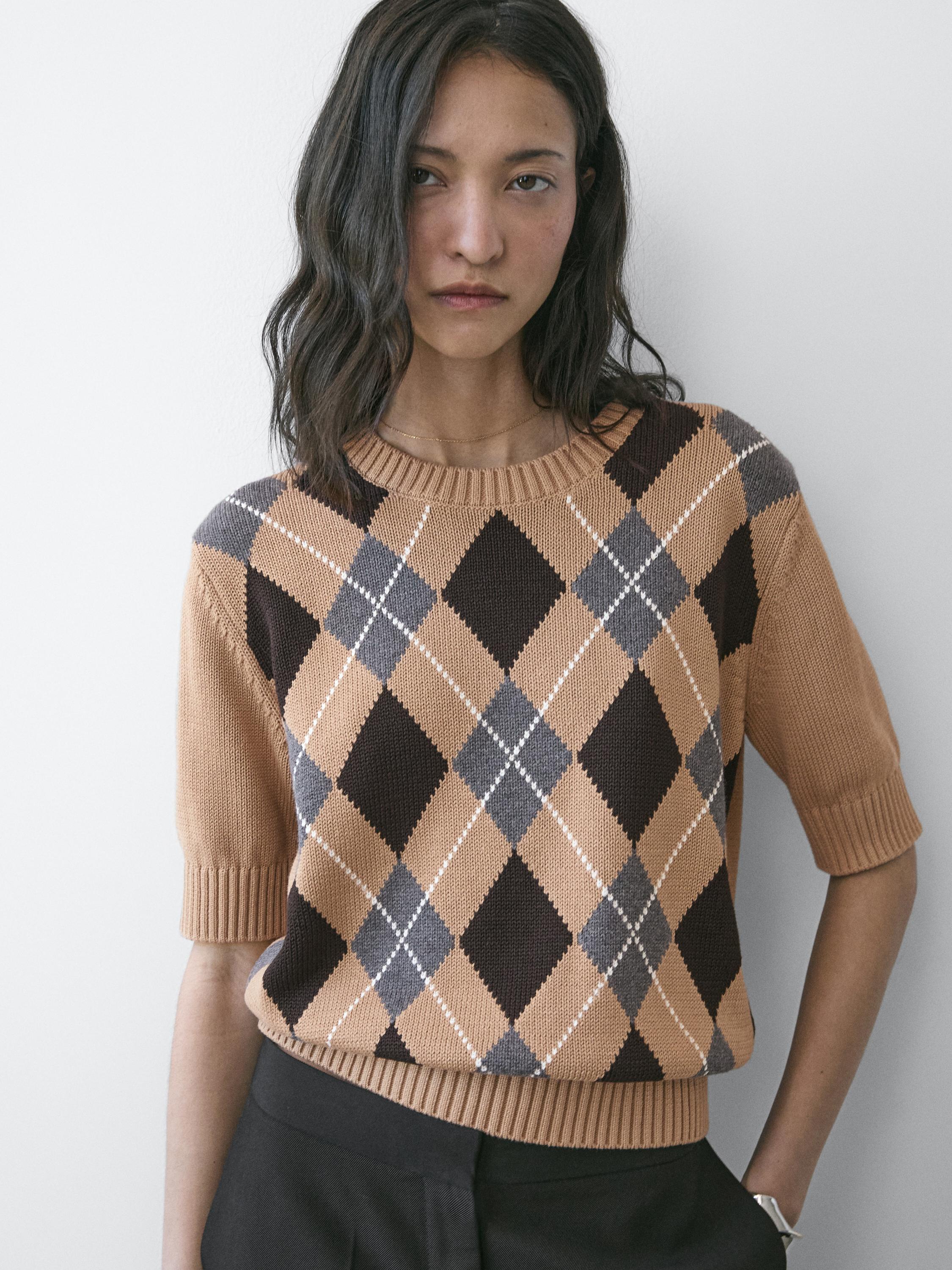 Close-up of a camel sweater with brown and gray argyle, short sleeves, and a round neck.