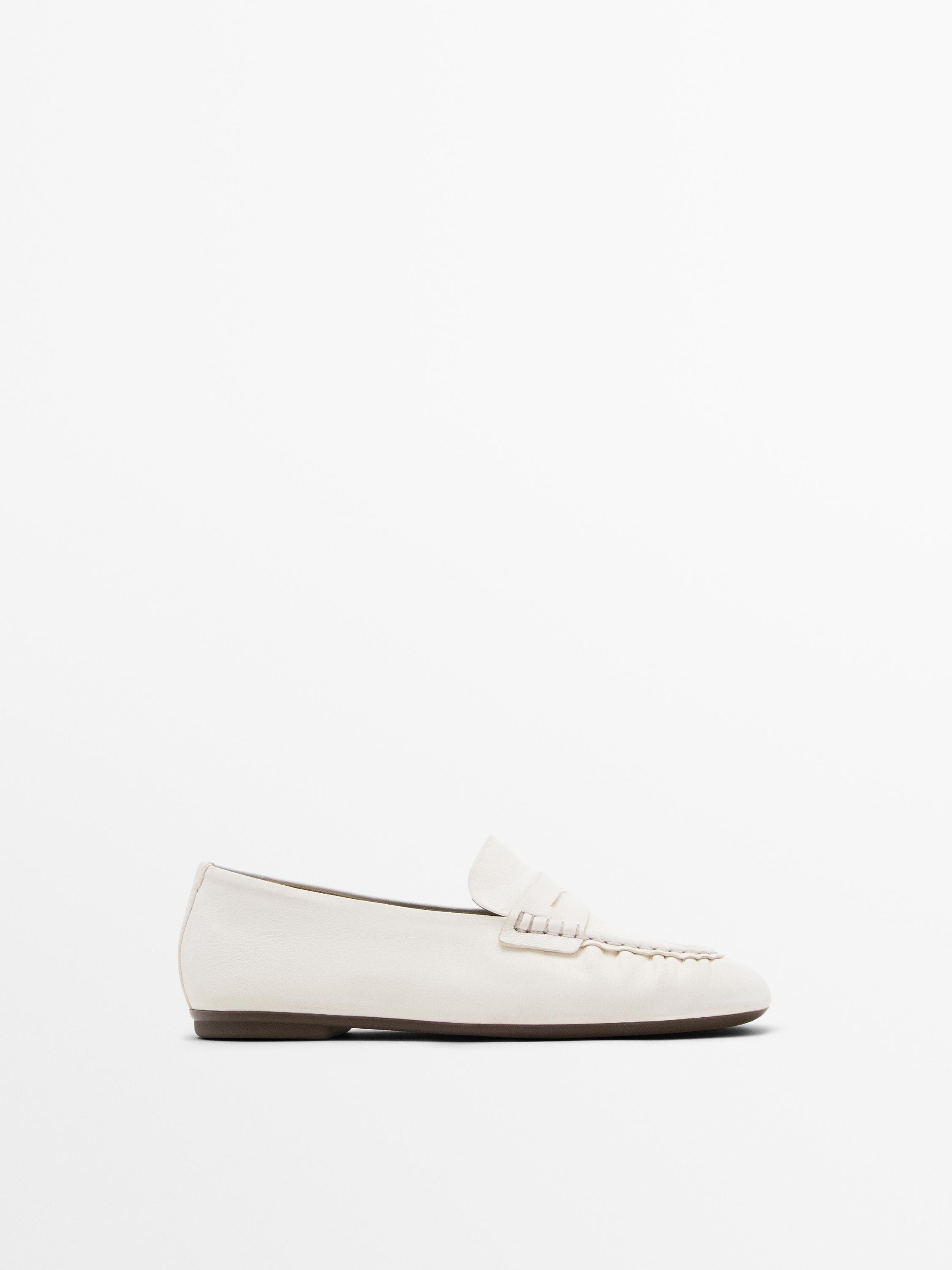 Side view of a white loafer with instep detail and brown flat sole.
