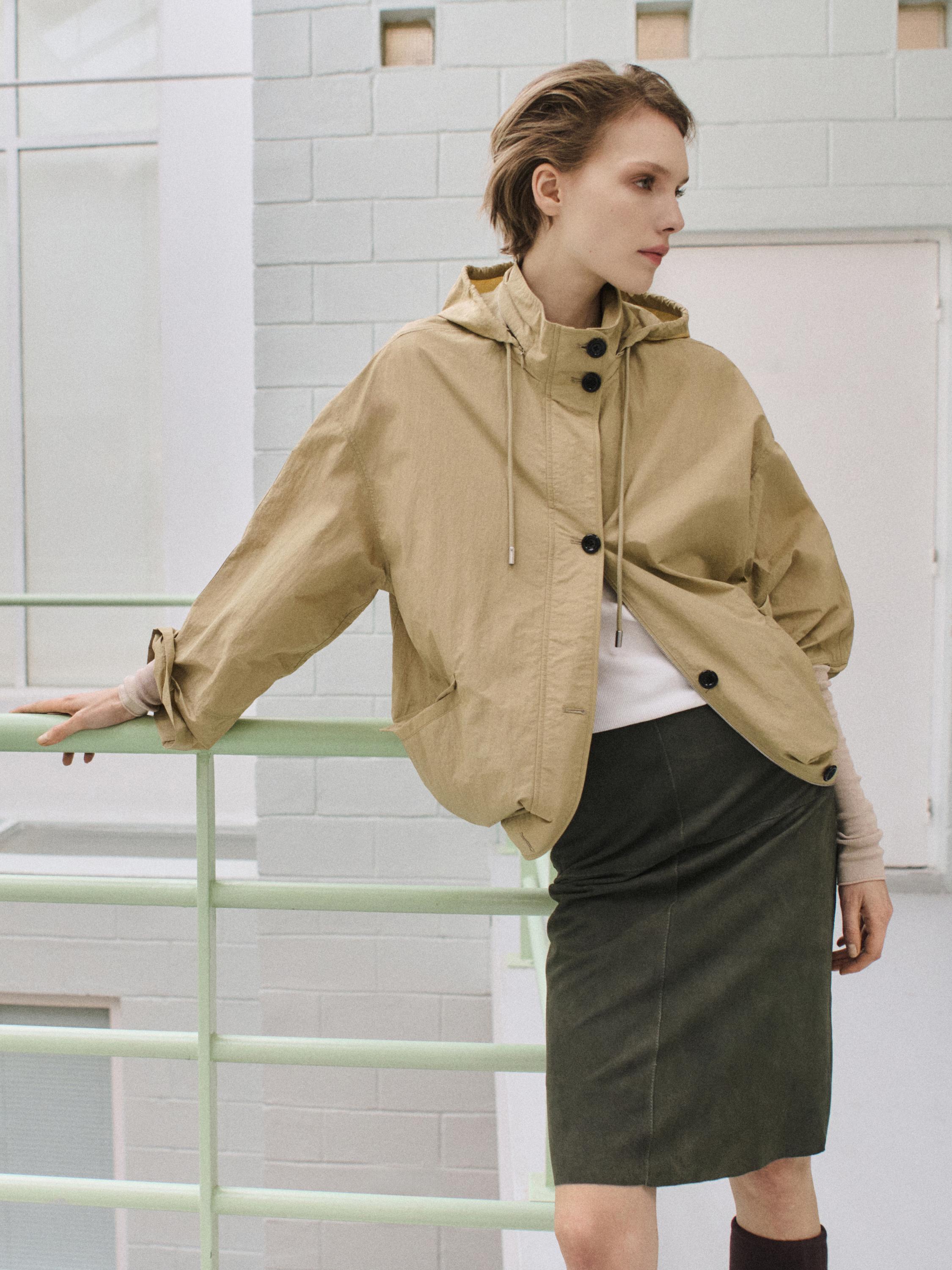 Light beige parka set with a hood and large buttons, dark green pencil skirt, and white t-shirt.
