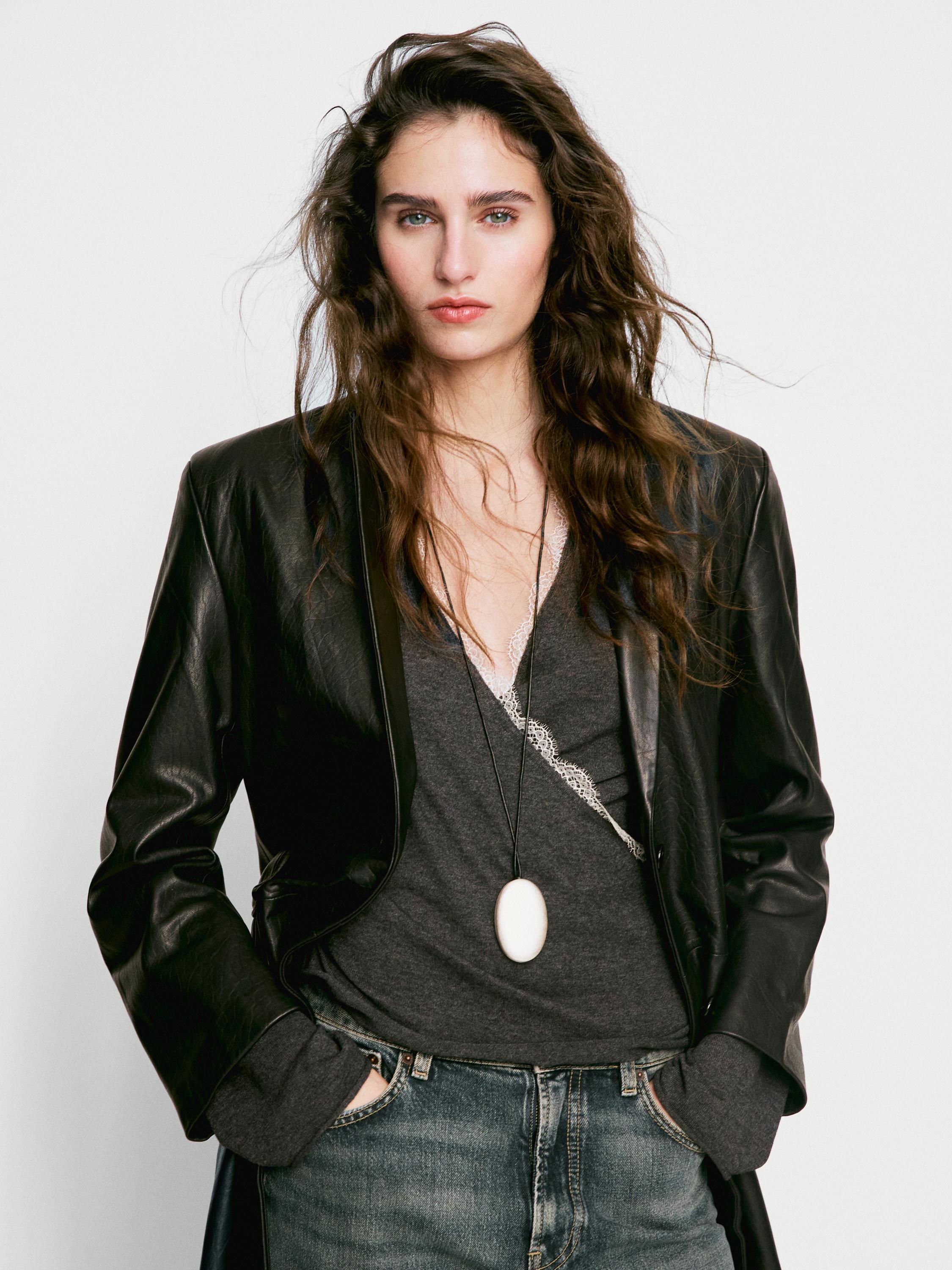 Plano medio de chaqueta negra de cuero con camiseta gris debajo y jeans azules. Bolsillos laterales visibles.