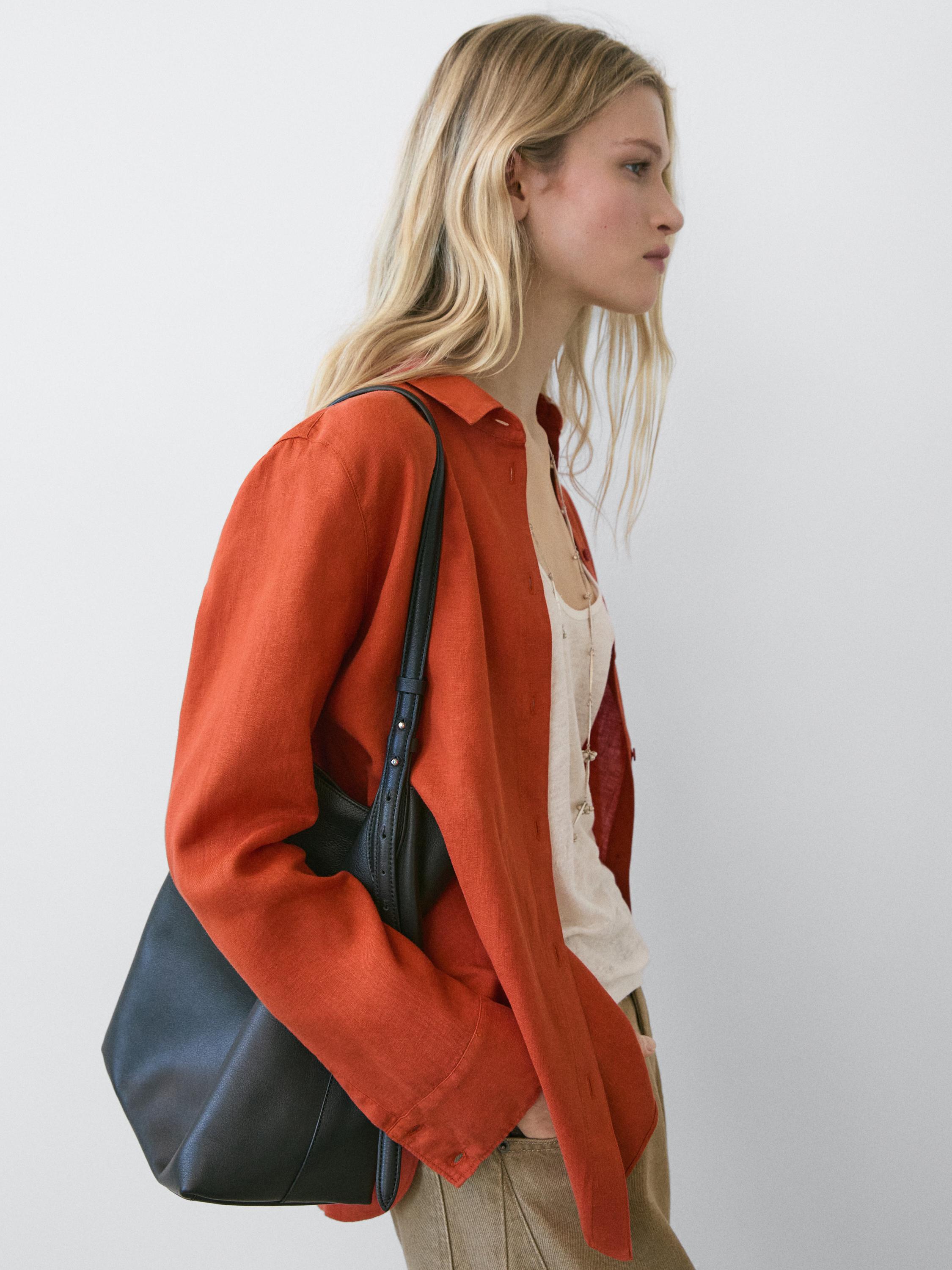 Halflang shot van een oranje, soepelvallend overhemd met klassieke kraag en lange mouwen, over een wit T-shirt.