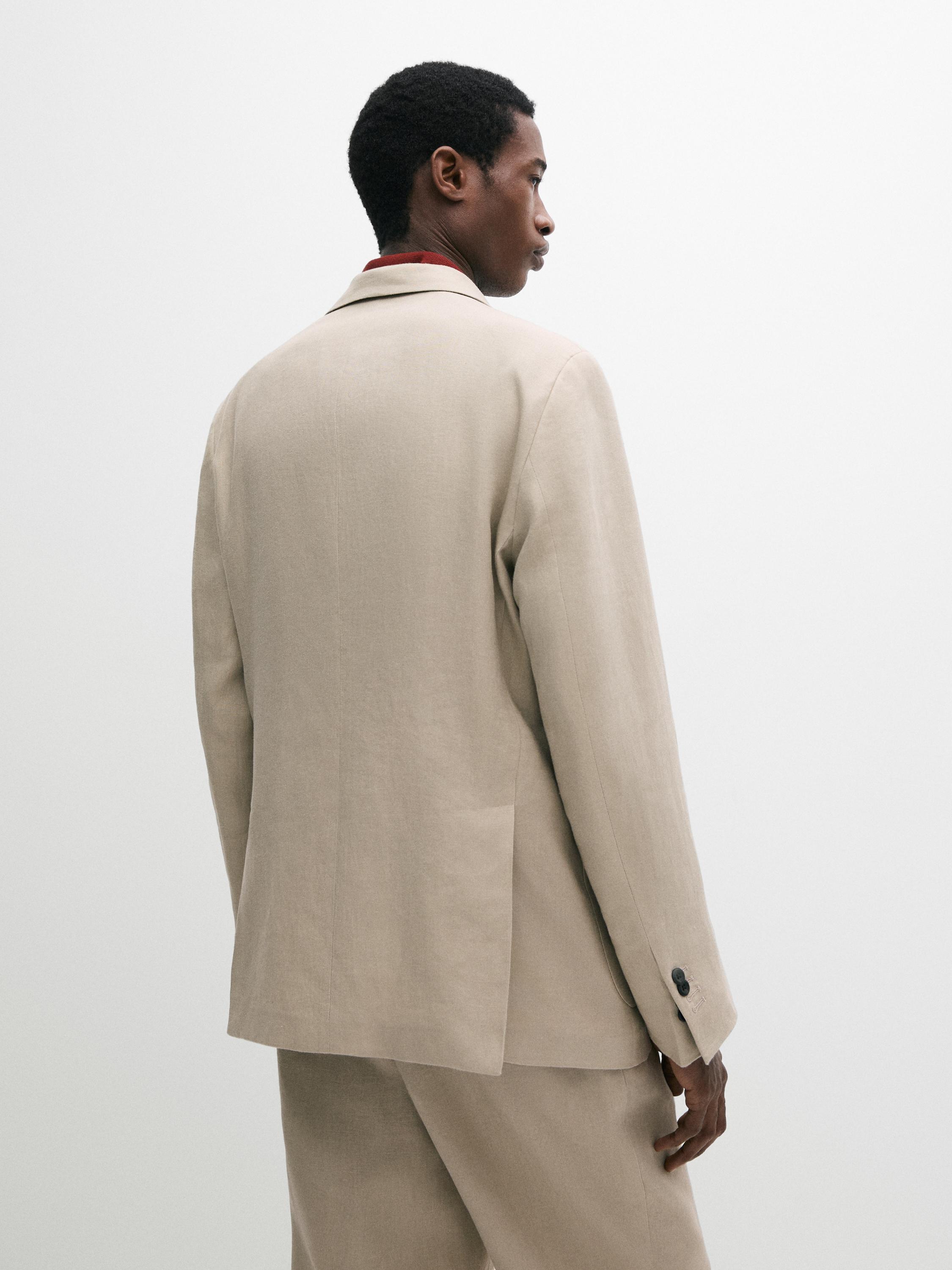 Rear view of a beige casual blazer with a classic lapel and a dark button on the sleeve.