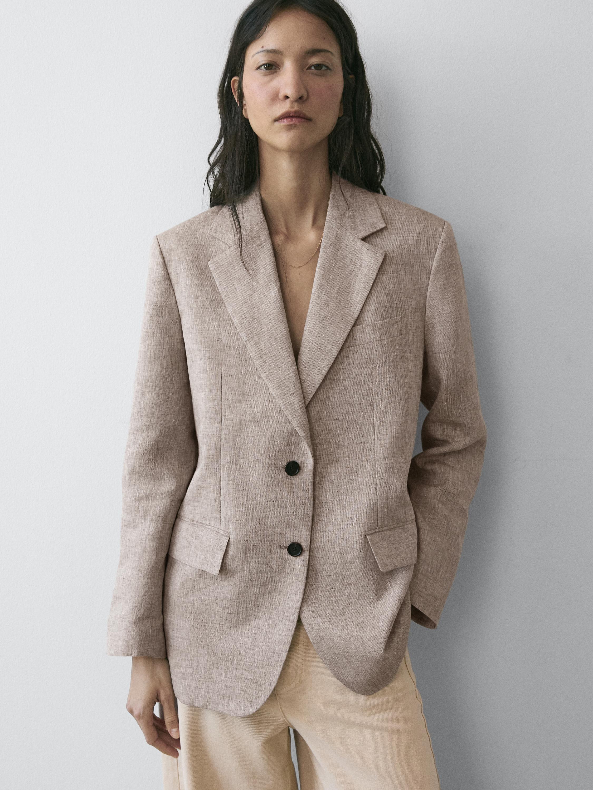 Beige blazer set with lapels, two black buttons, and flap pockets, paired with light-colored pants.