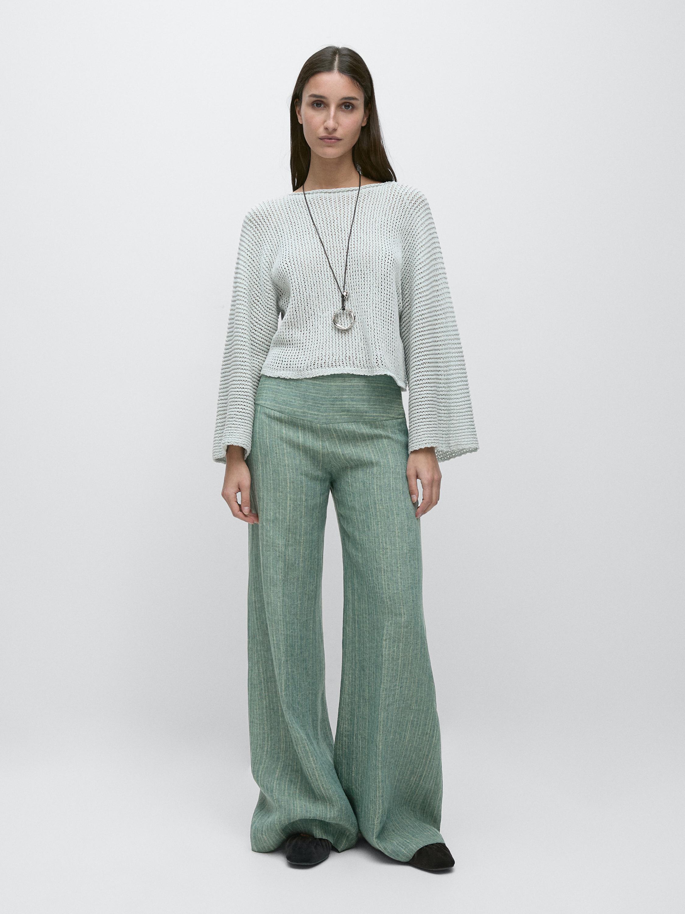 Conjunto de suéter blanco de manga larga y pantalones verdes de pierna ancha.