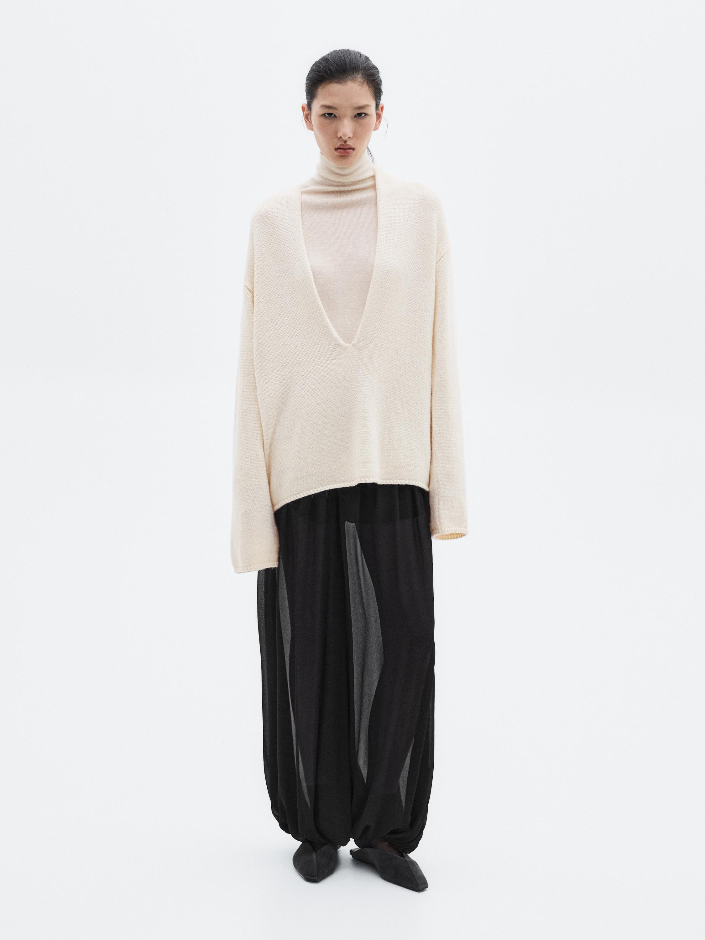 Beige sweater set with a deep neckline and wide, sheer black pants.