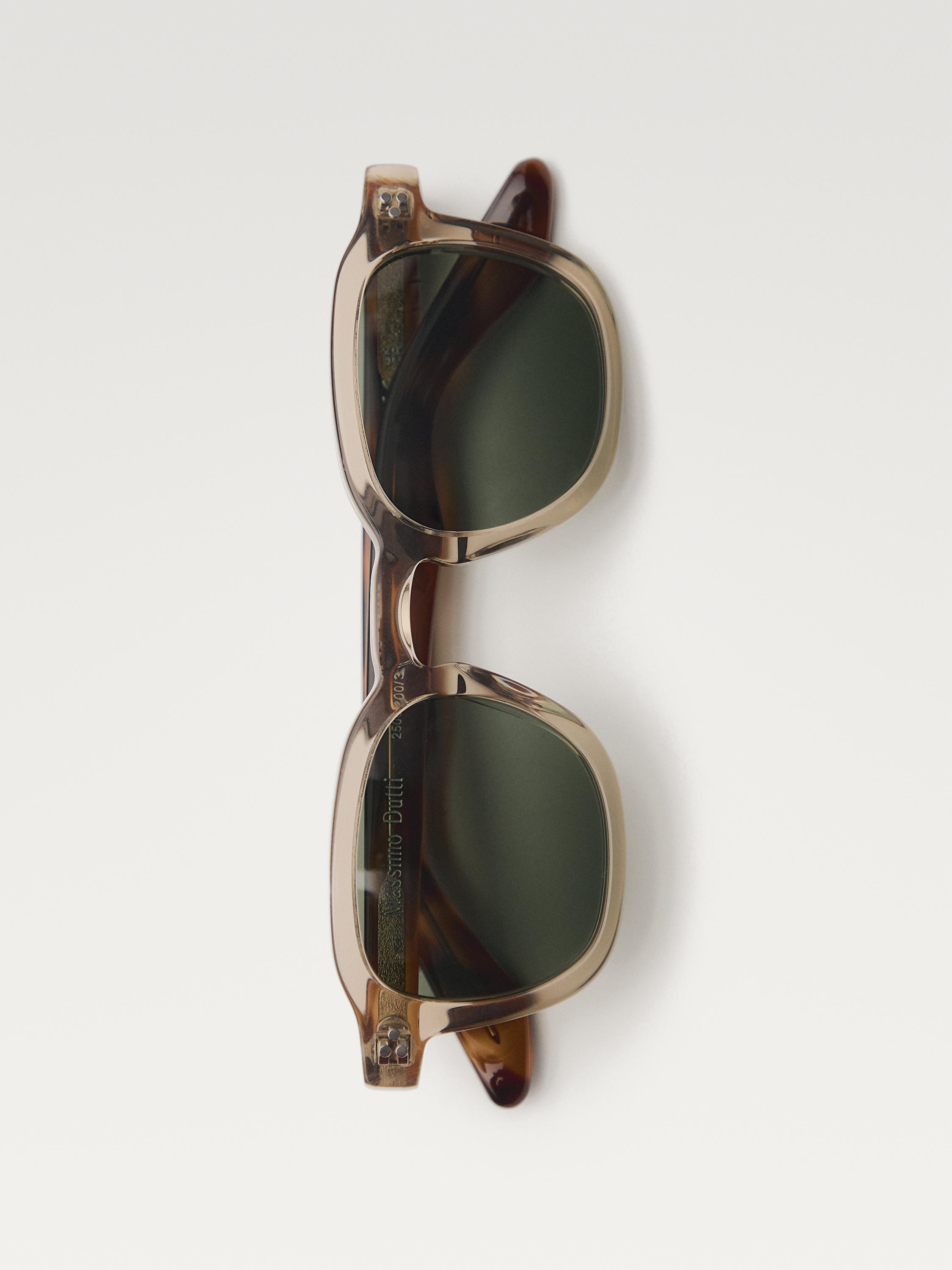 Vista frontal de gafas de sol amarillas con lentes oscuras y montura cuadrada. Texto visible en la patilla.