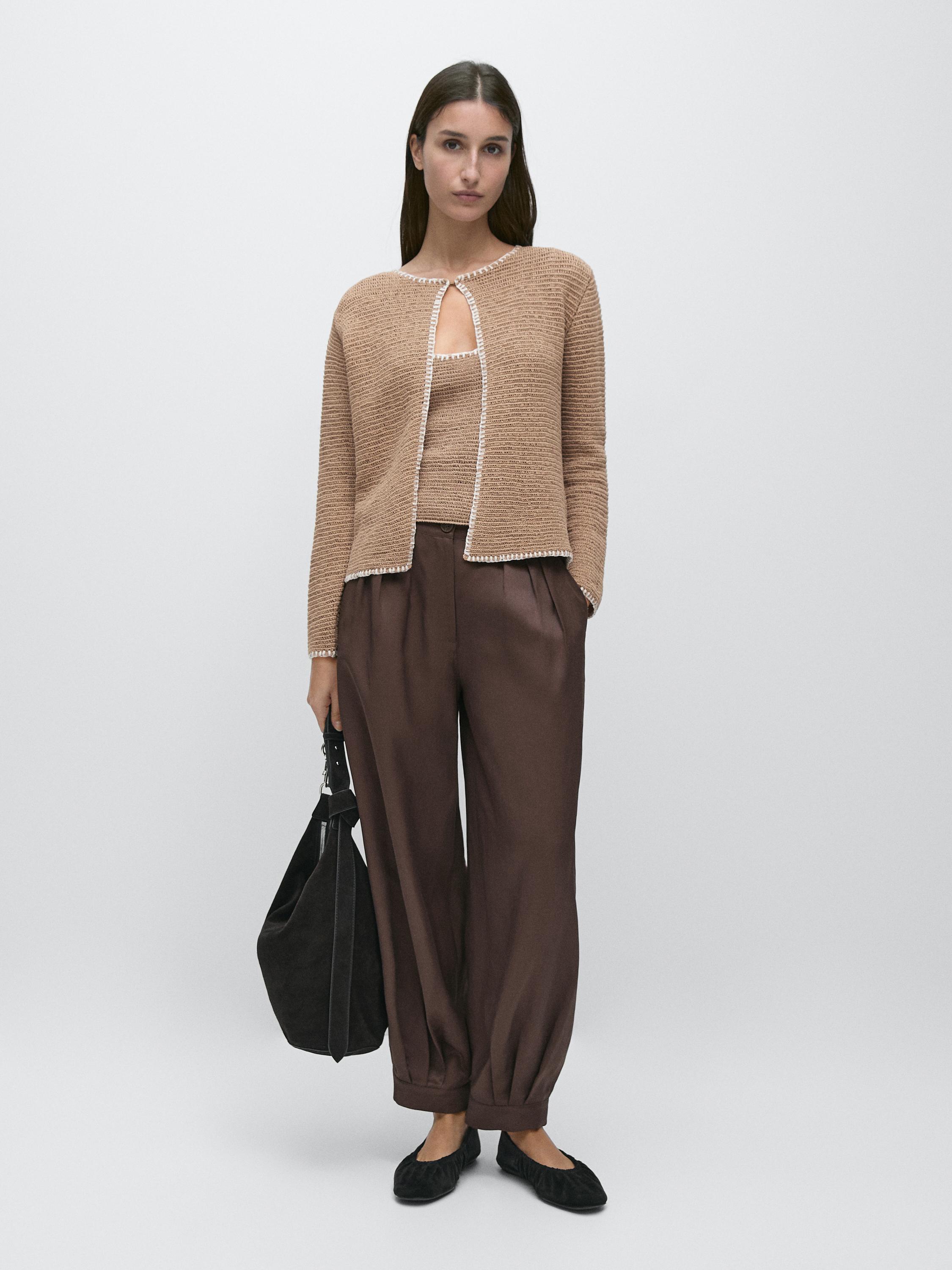 Bộ áo khoác cardigan màu be dáng mở có viền trắng, áo top đồng bộ, quần ống rộng màu nâu và giày đen.