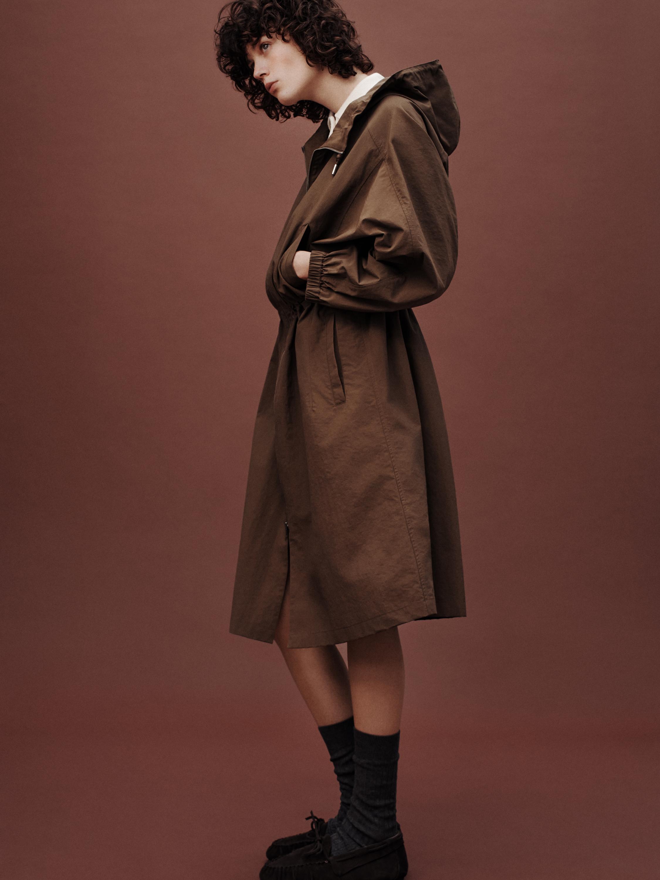 Коричневое пальто с капюшоном и боковыми карманами, белая рубашка, серые носки и черные мокасины.