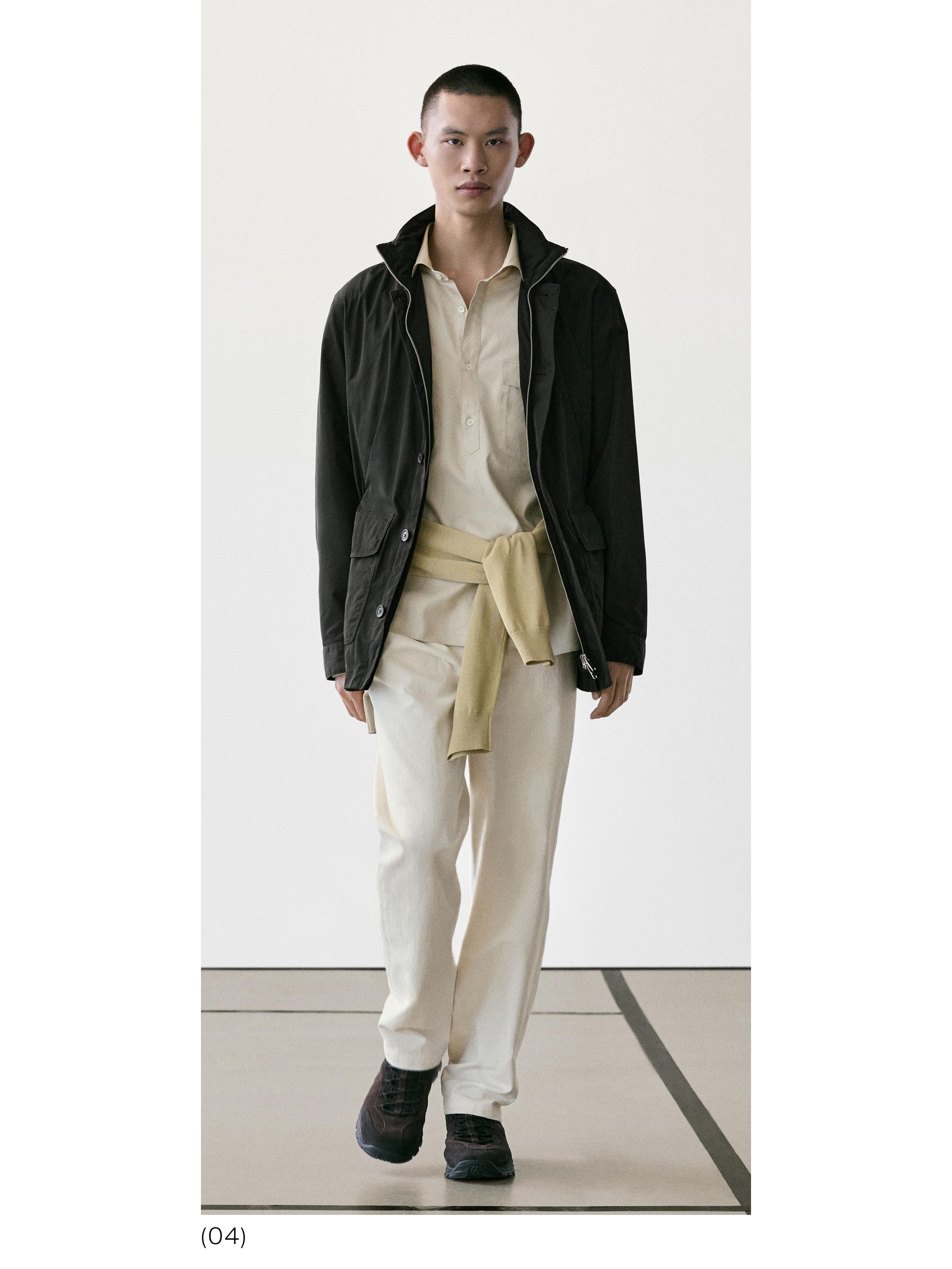 Conxunto de chaqueta negra con petos, camisa beis, pantalóns claros e xersei amarelo atado á cintura.