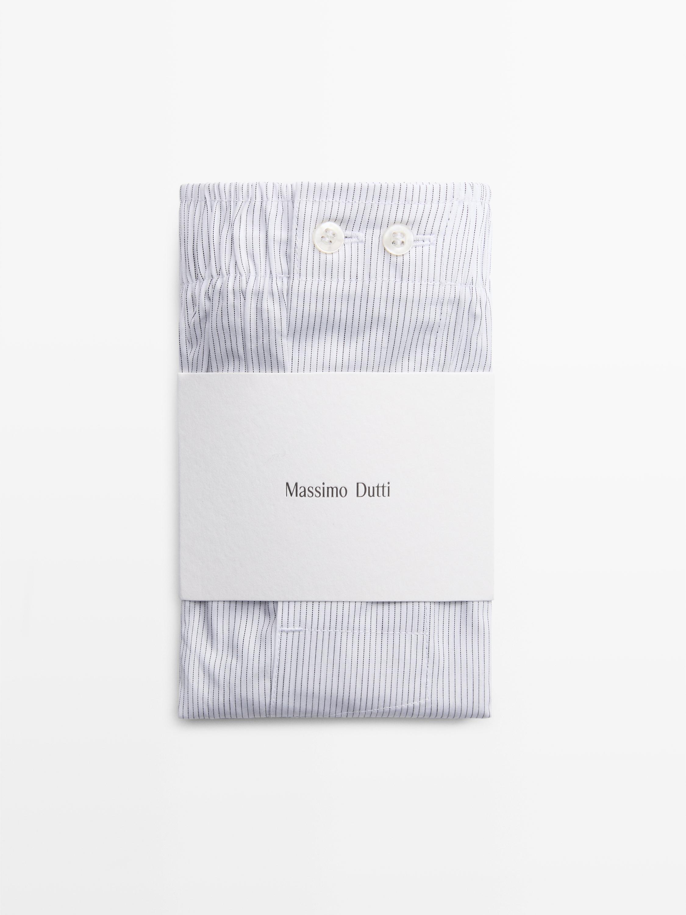 "Prednji pogled na bele bokserice sa tankim prugama i dva vidljiva dugmeta na pojasu. Tekst 'Massimo Dutti' na pakovanju."