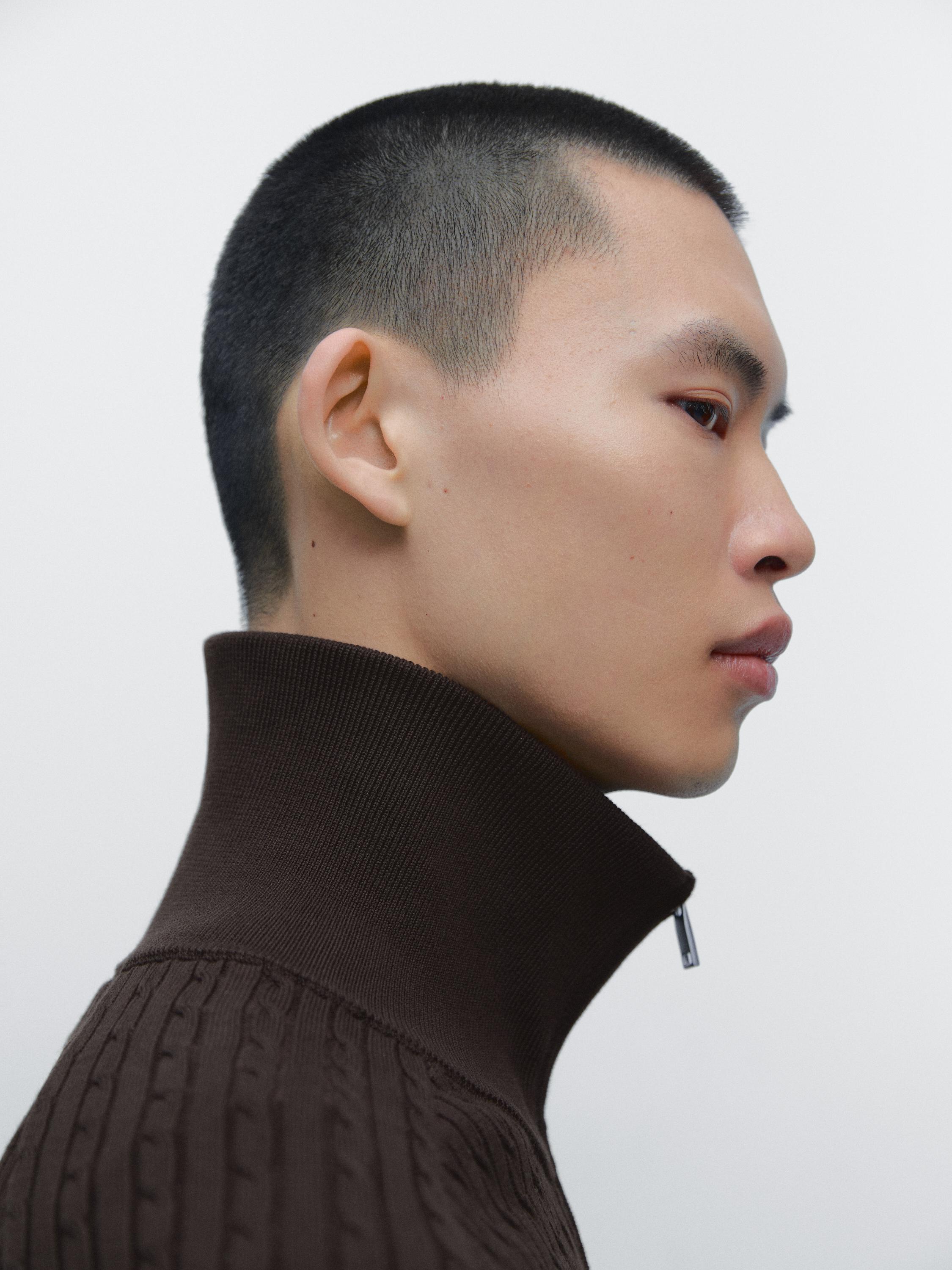 Деталь: воротник-стойка на молнии на меланжевом коричневом кардигане крупной вязки.