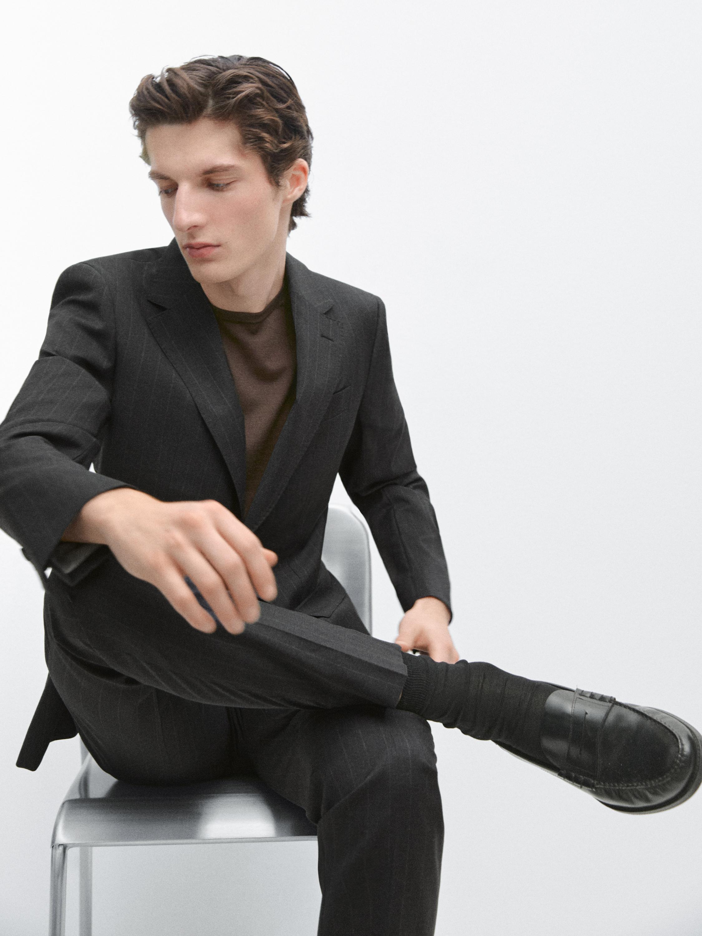 Grauer Anzug mit maßgeschneidertem Sakko und passender Hose, darunter ein braunes T-Shirt.