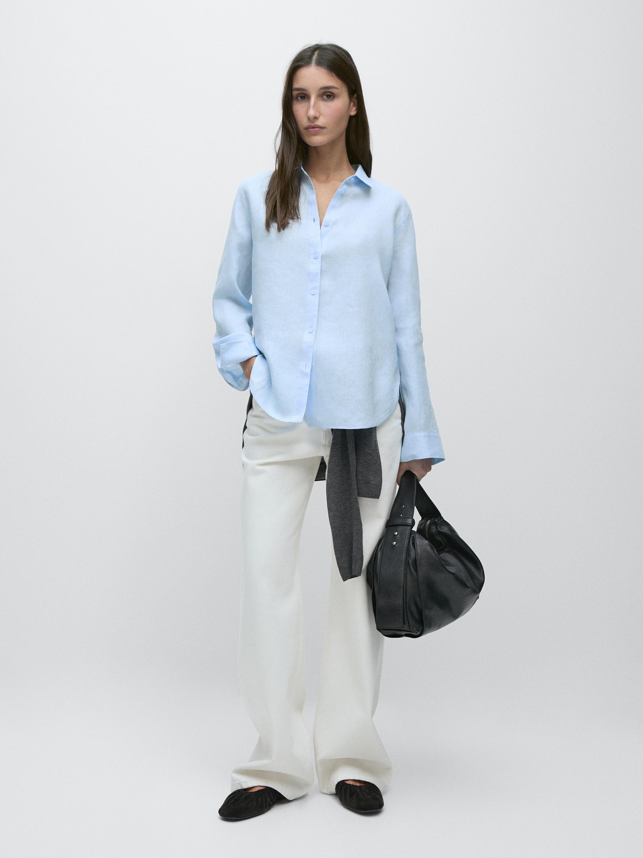 Set aus hellblauem Hemd mit Knöpfen, weiter weißer Hose und schwarzer Tasche.