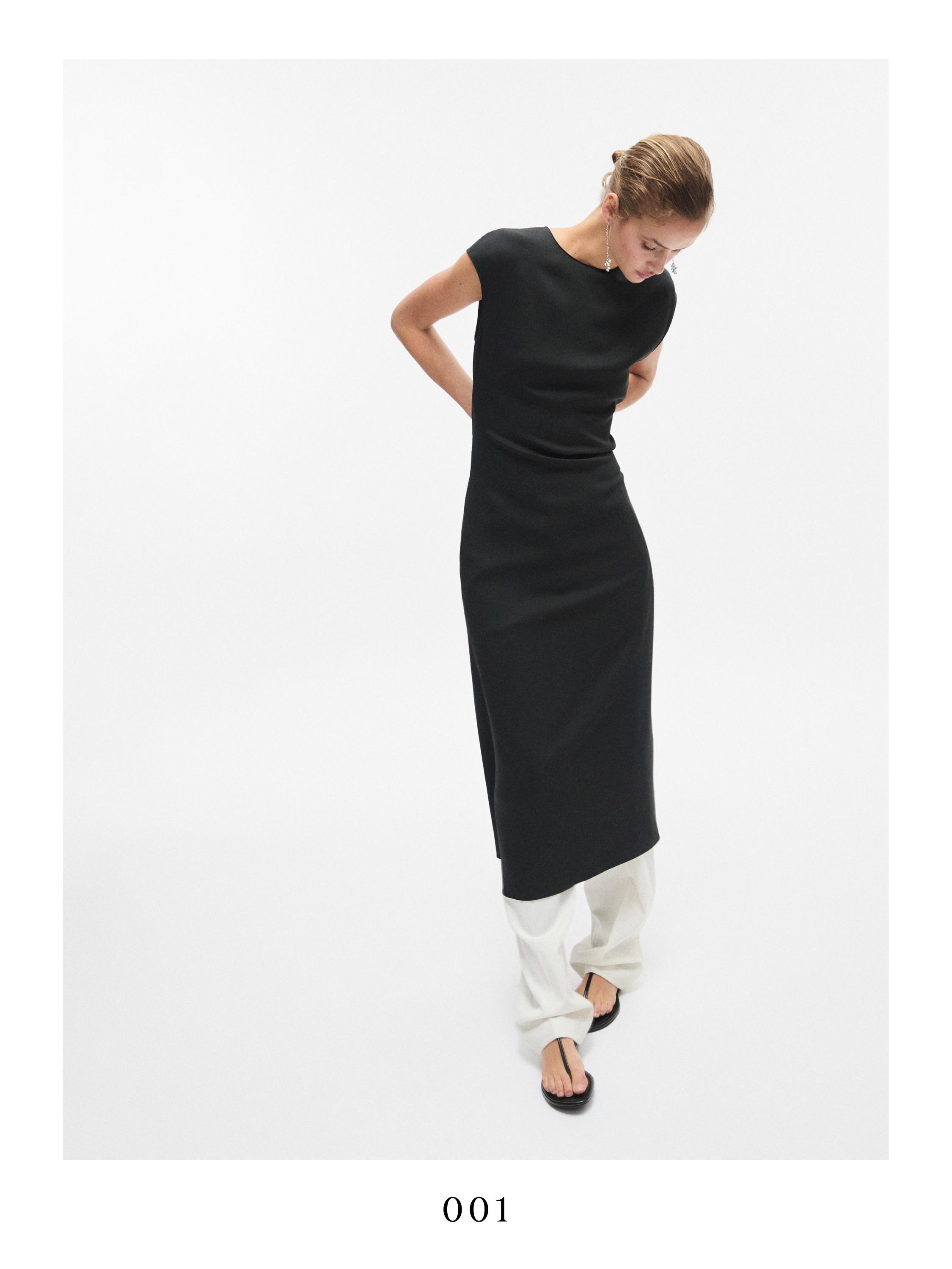 Σετ με ρέον μαύρο φόρεμα με κοντά μανίκια πάνω από λευκό παντελόνι, ορατά μαύρα σανδάλια.