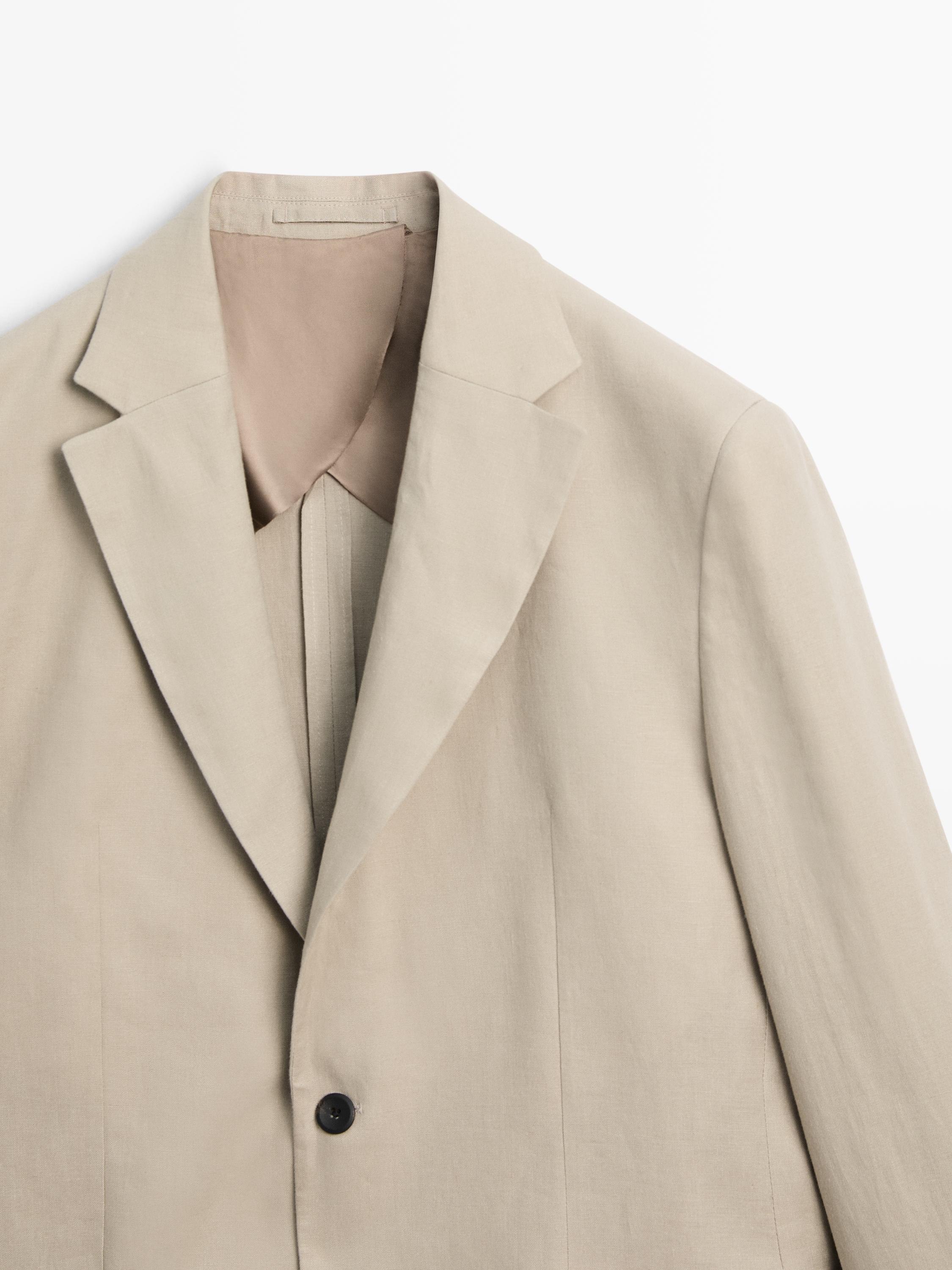 Plano mitjà de blazer beix amb solapa clàssica i un botó negre visible.