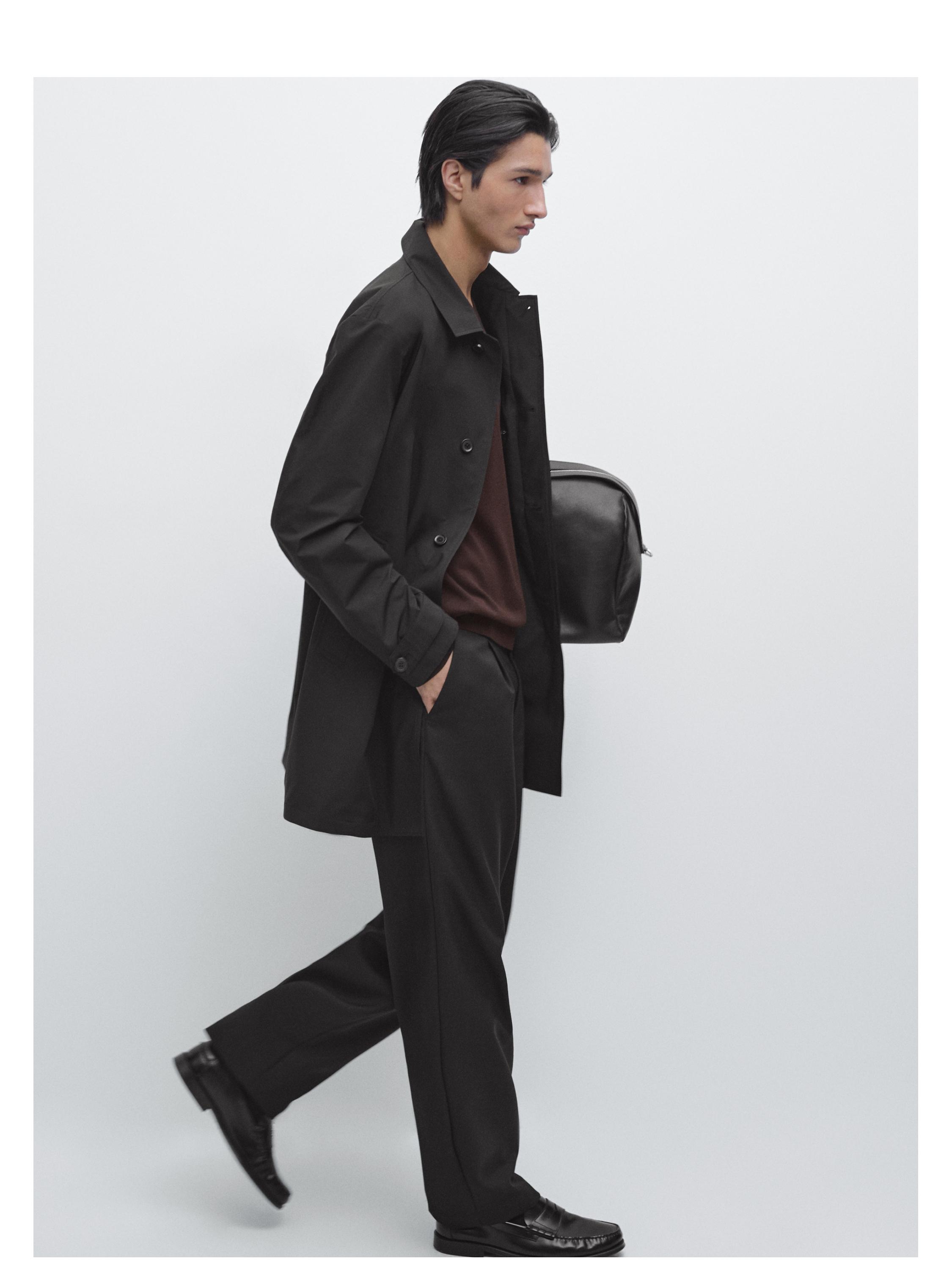 Sæt med sort parka med knapper, sorte bukser og sorte sko. Brun T-shirt synlig. Sidelomme synlig.