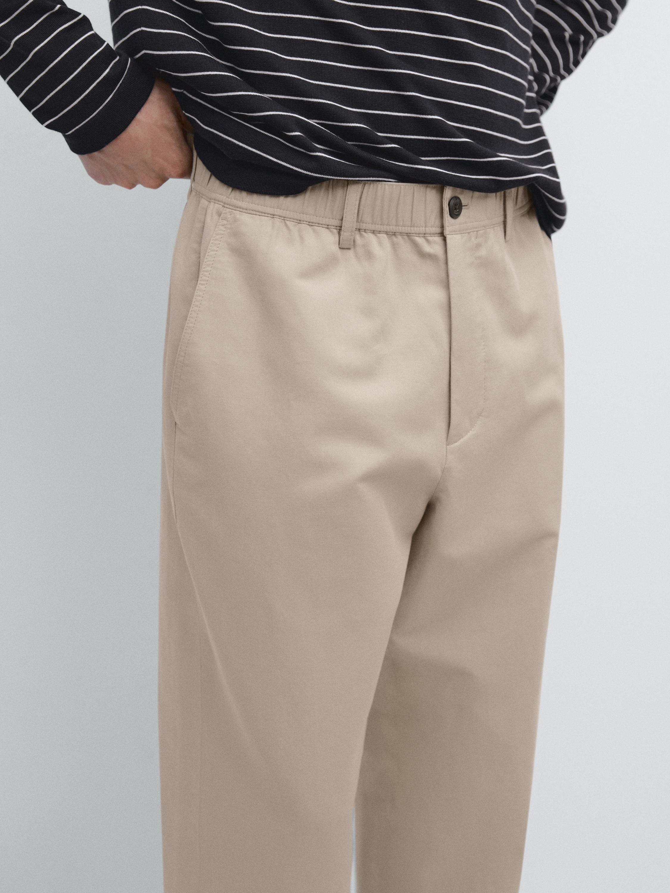 Plano medio de pantalón beige con bolsillos laterales y cintura elástica con botón.