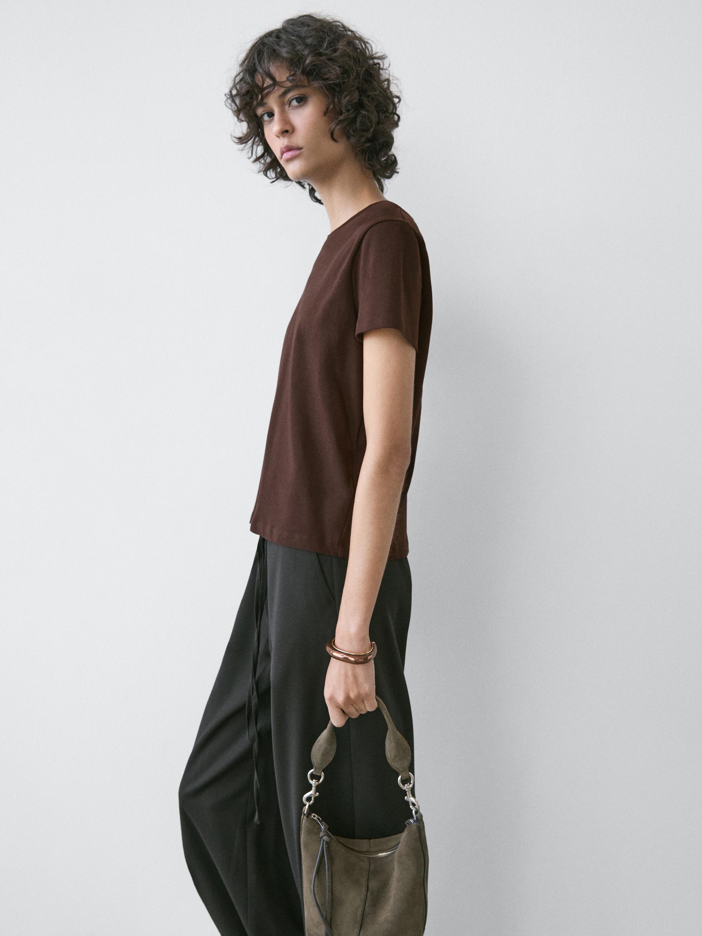 Plano medio di maglietta marrone a maniche corte e pantaloni neri.