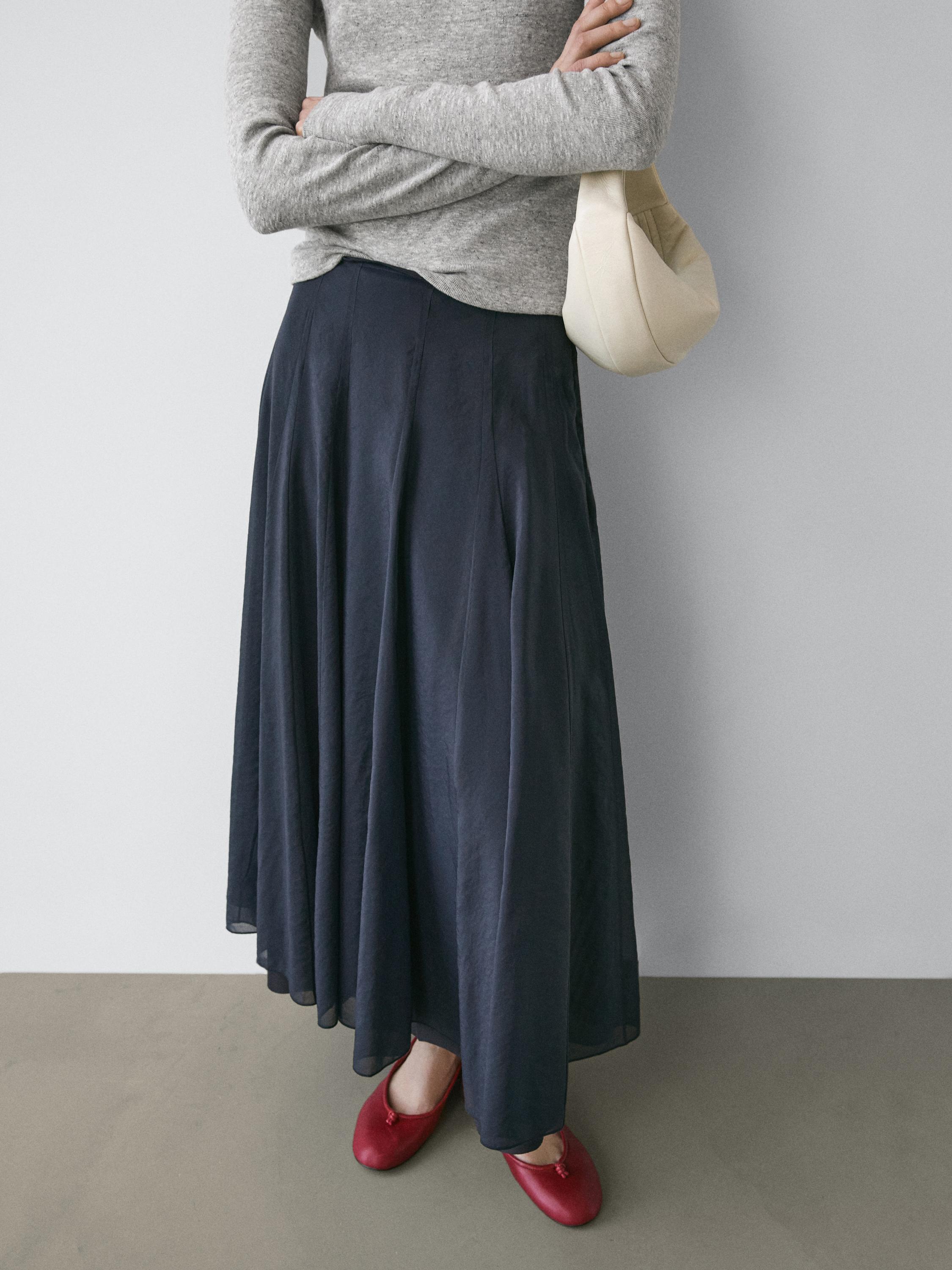 Mid-shot of a dark blue midi skirt with pintucks, paired with a gray sweater and red shoes.