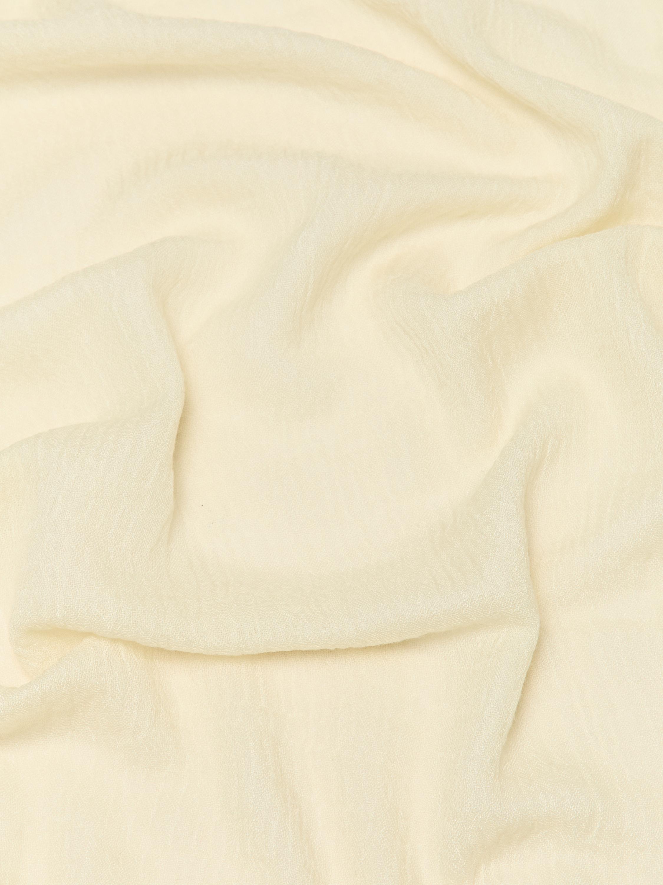 Detalle de tela de pañuelo amarillo con textura suave y pliegues visibles.
