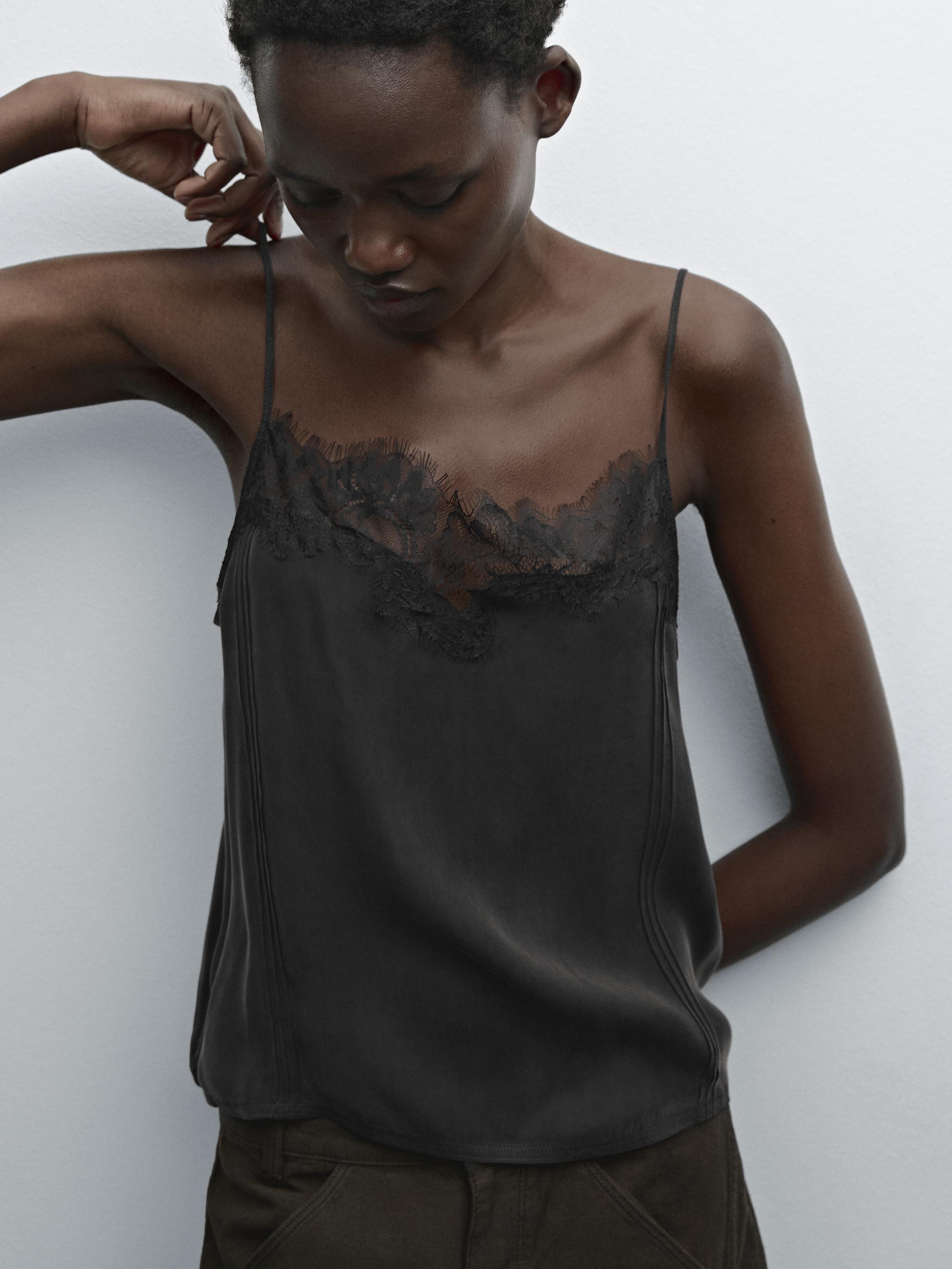 تفاصيل بلوزة سوداء بحمالات رفيعة ودانتيل على فتحة الصدر.