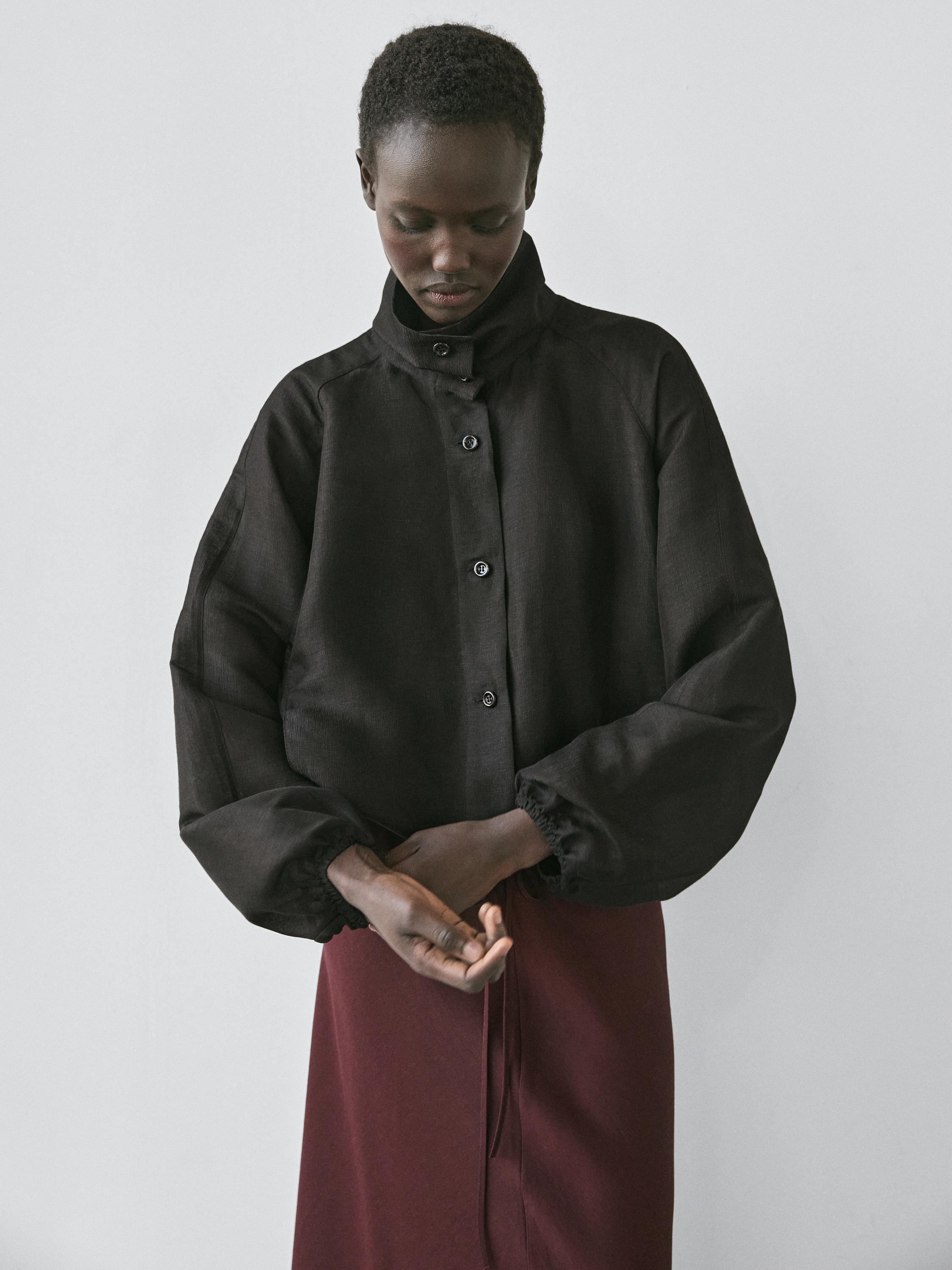 ภาพระยะกลางของแจ็คเก็ตบอมเบอร์สีดำ คอตั้ง มีกระดุมด้านหน้า แขนยาวพร้อมข้อมือยางยืด