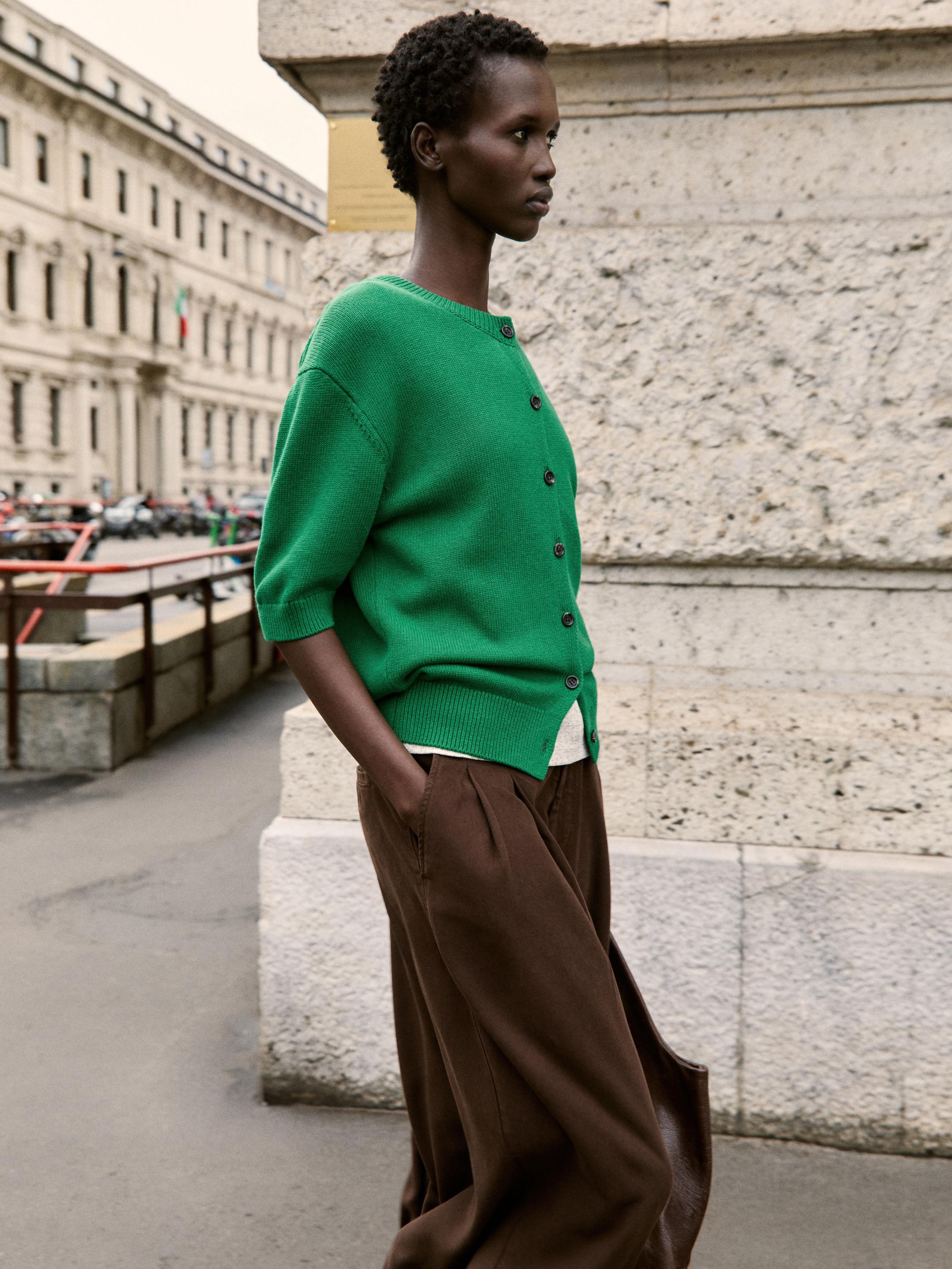 Ensemble gilet boutonné vert et pantalon marron à poches latérales.