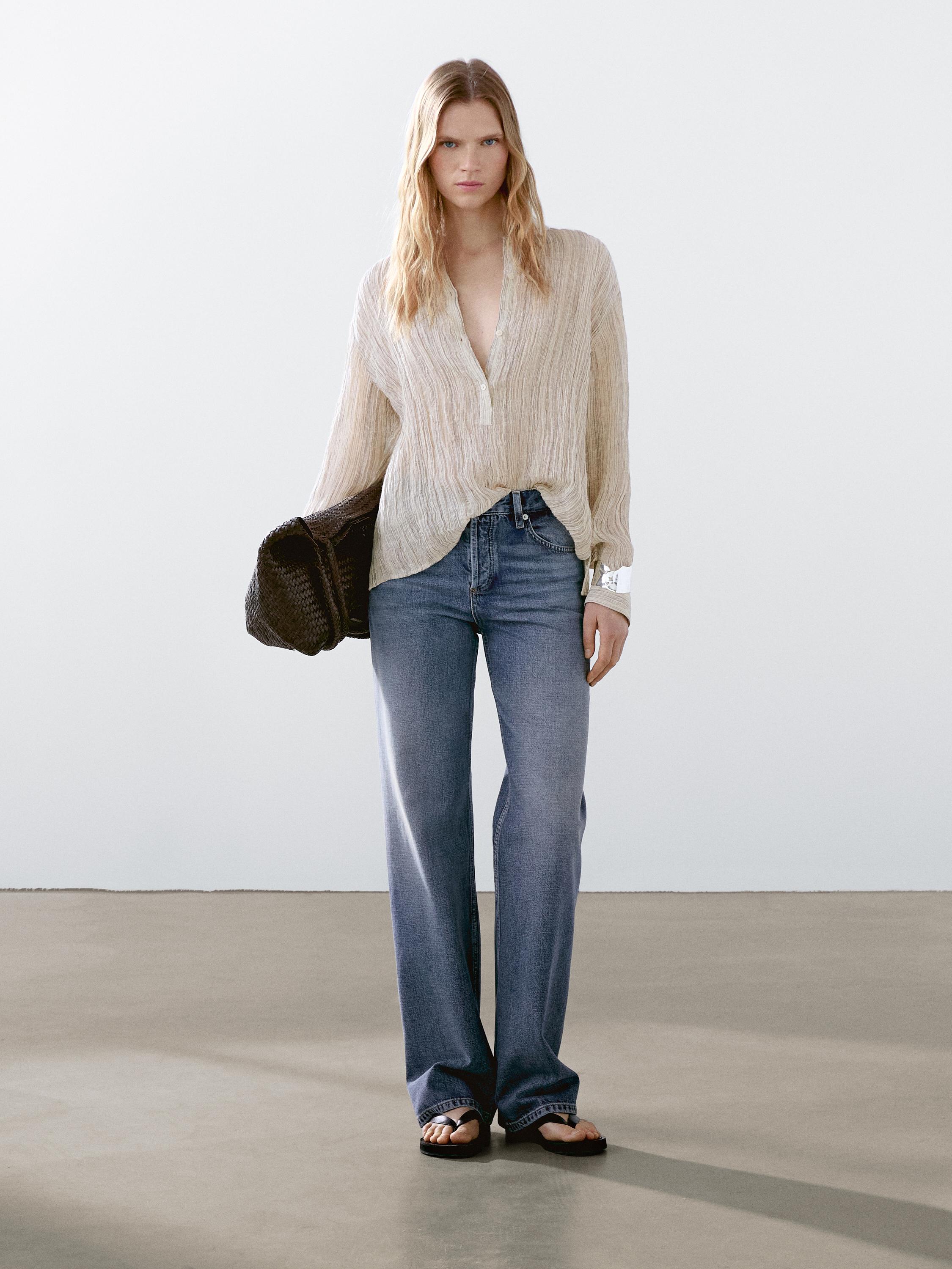 طقم مكون من بلوزة بيج بأكمام طويلة وبنطلون جينز أزرق بقصة مستقيمة.